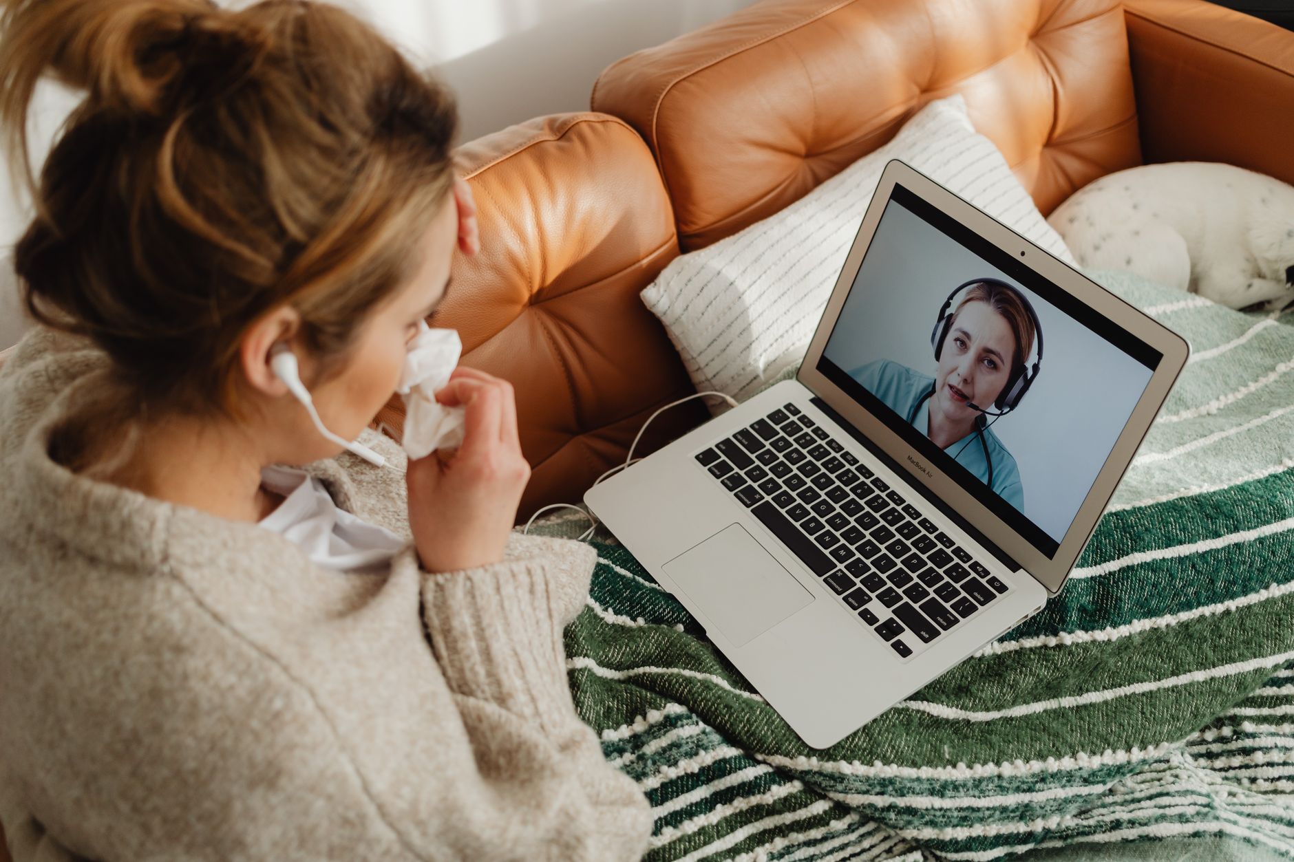 A patient sitting on a couch attending a video consultation on a laptop, feeling unwell.