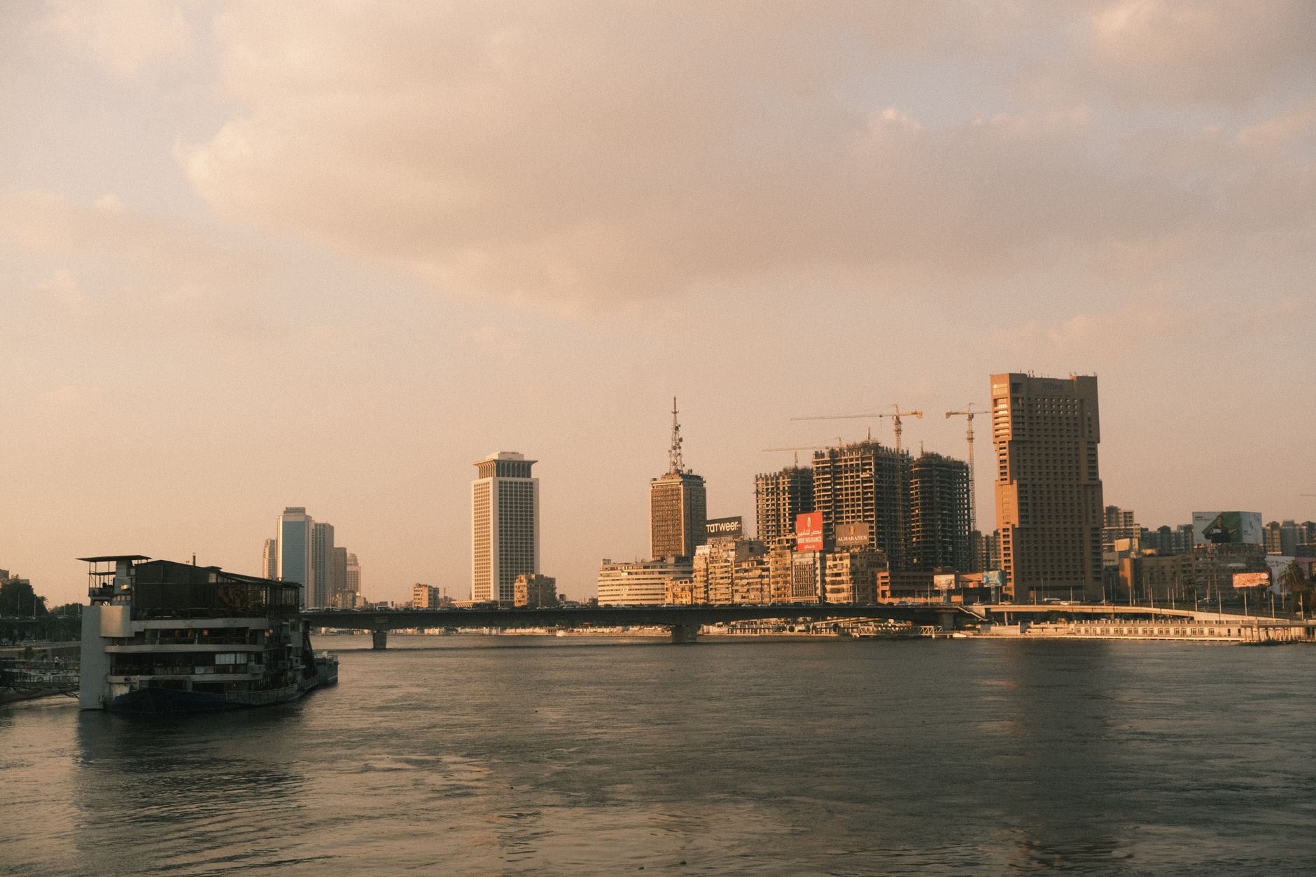 Cairo skyline featuring modern buildings and construction along the Nile River at sunset.
