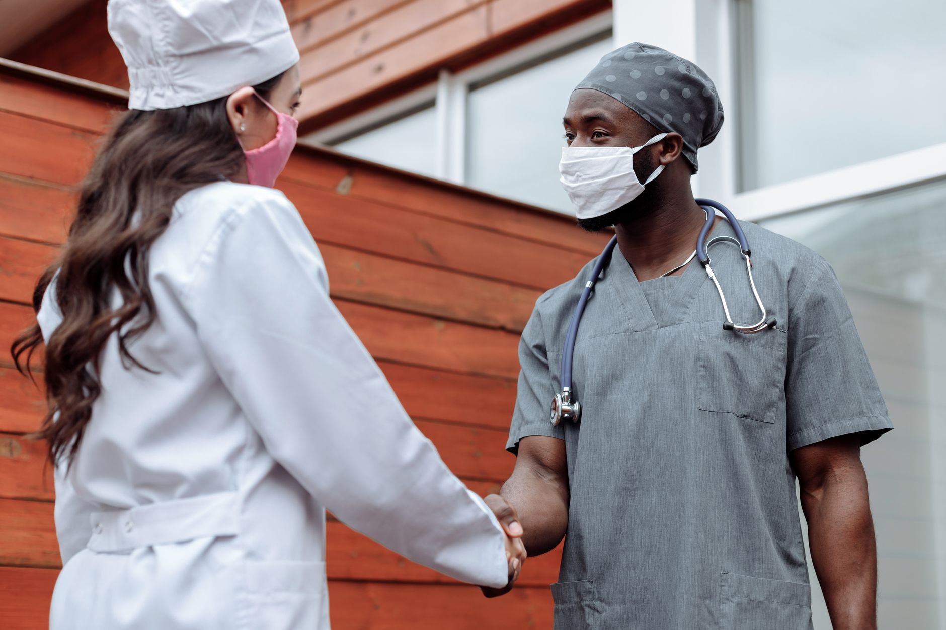 Two healthcare professionals shaking hands outdoors, symbolizing collaboration.