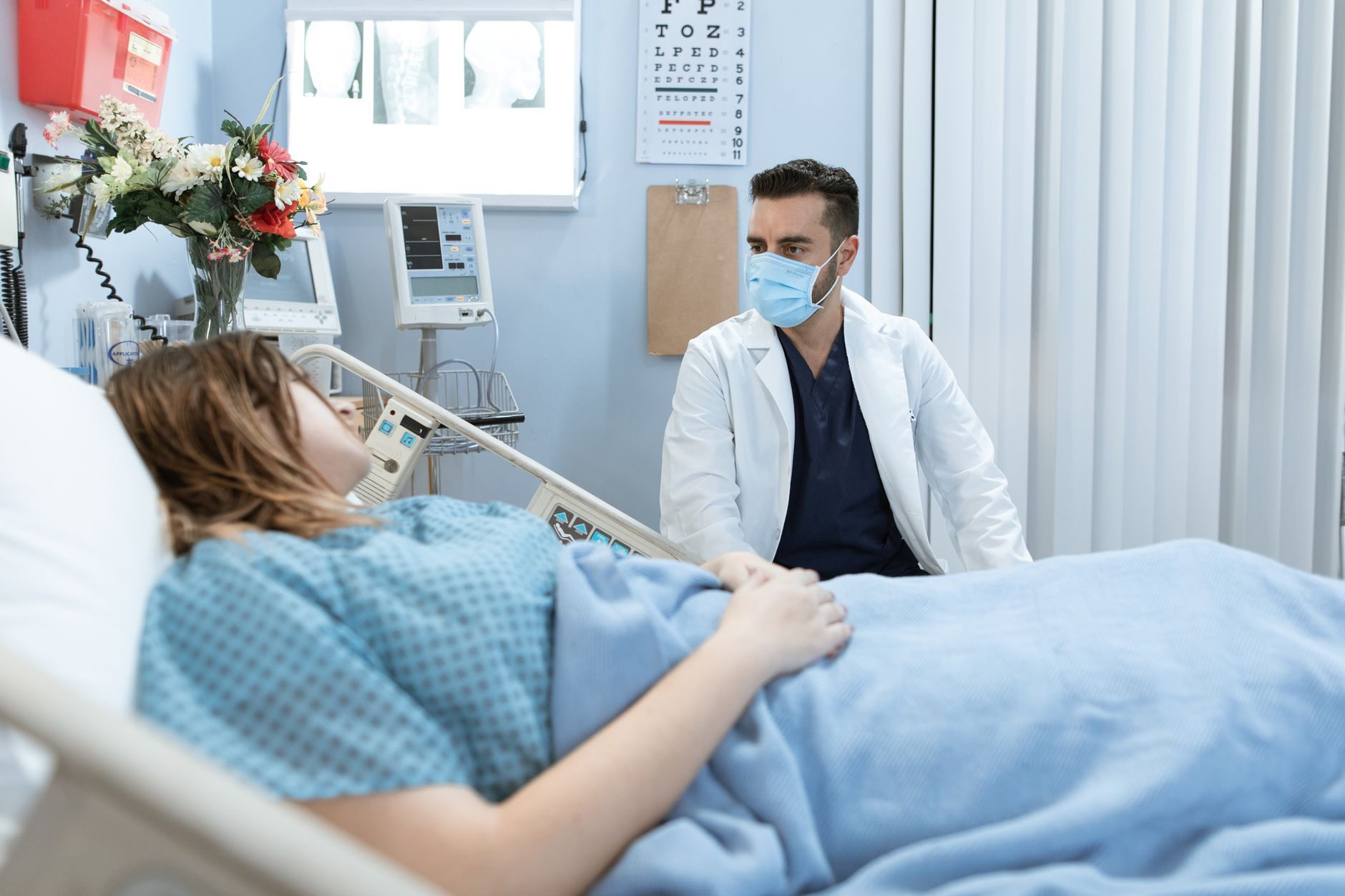 A doctor in a white coat talks to a patient in a hospital room.