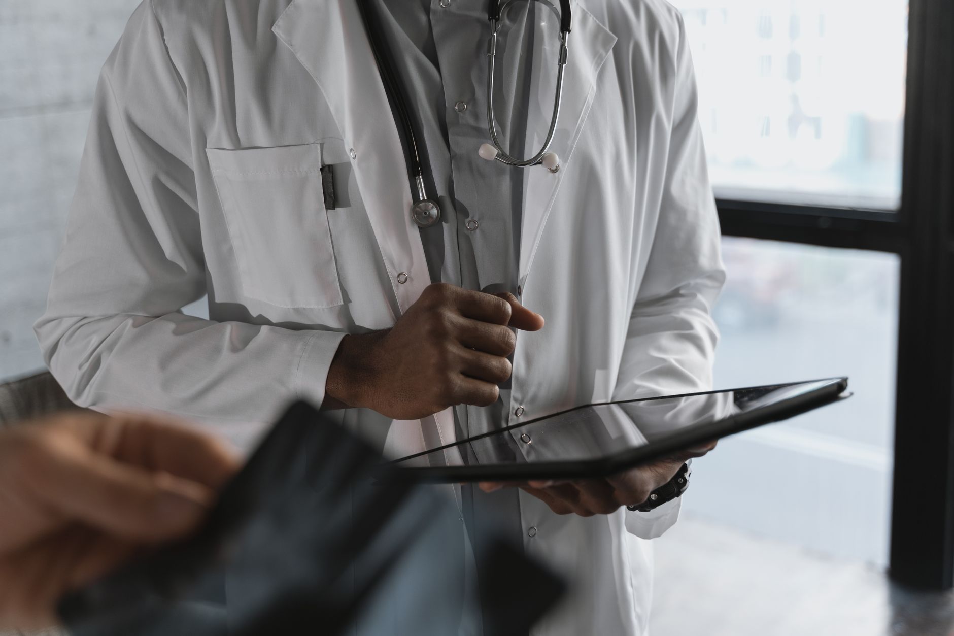 Doctor in a white coat holding a tablet, engaged in a telehealth appointment.