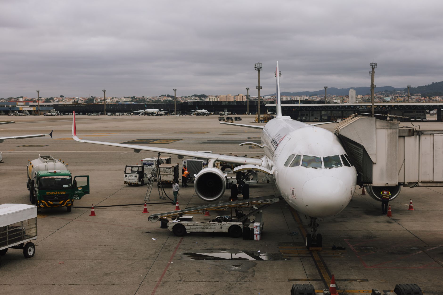 Aircraft at an airport with ground crew loading luggage near a terminal.