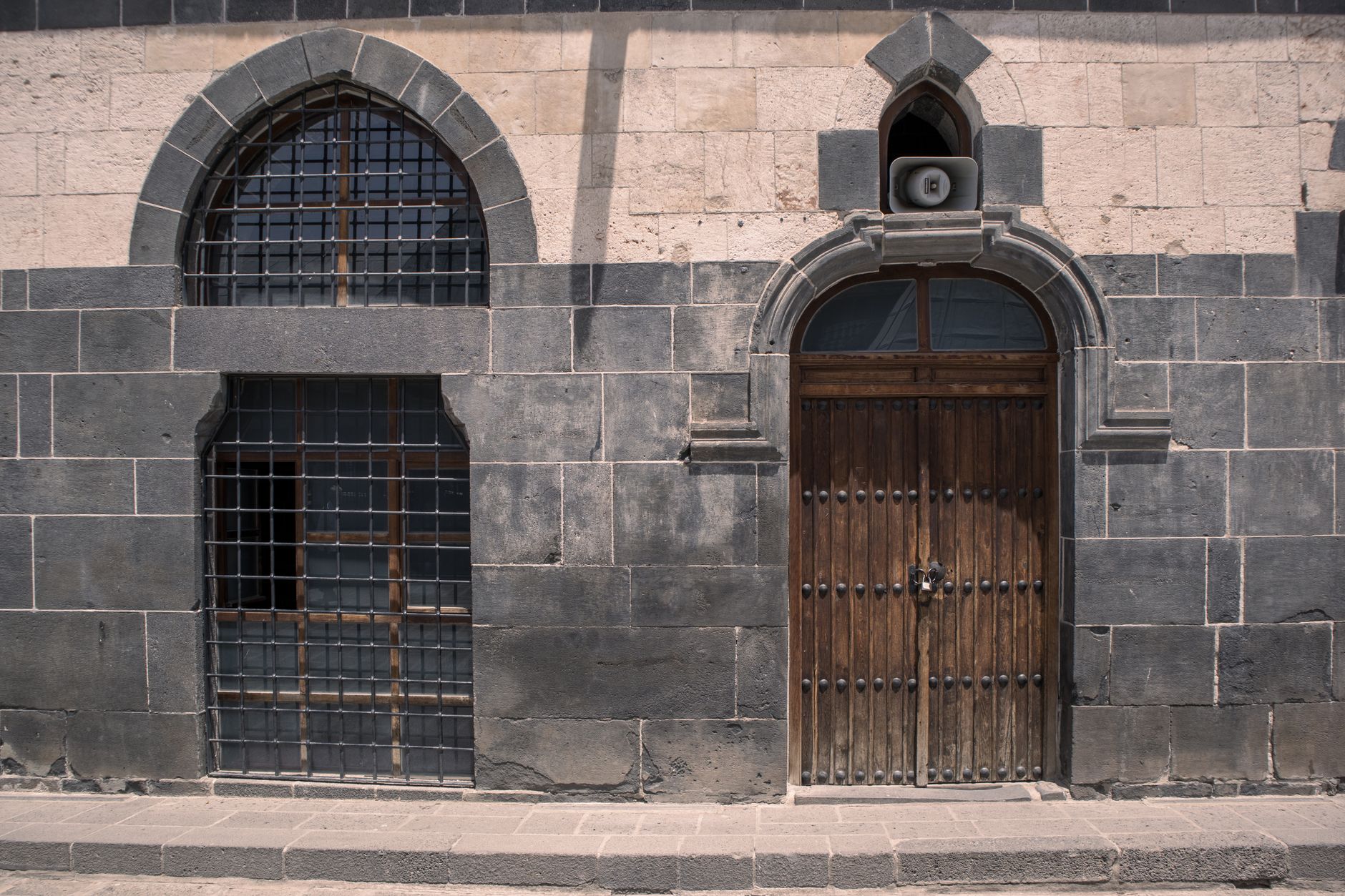 نمای نزدیک از یک دیوار سنگی بازالتی در دیاربکر، با یک پنجره میله‌دار و یک در چوبی.