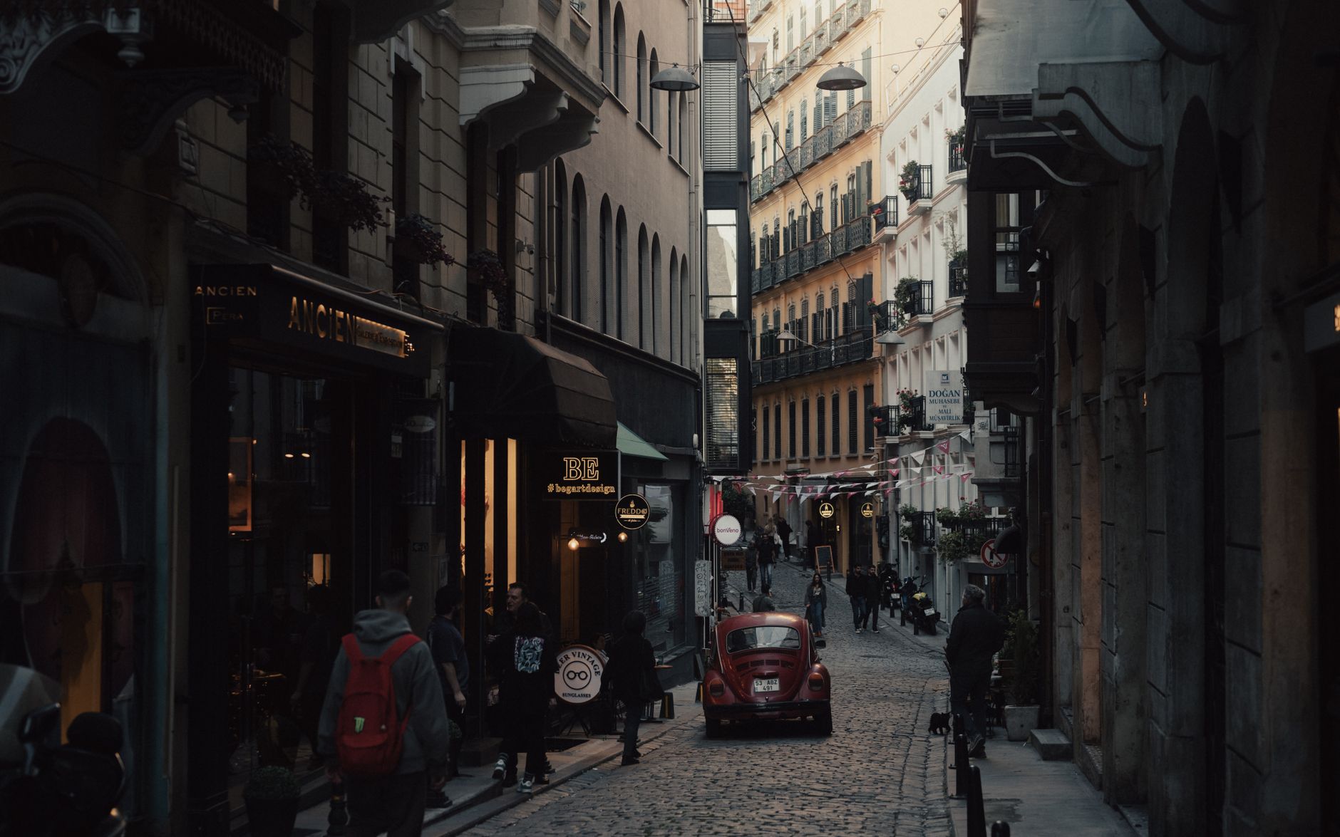Narrow cobblestone street in Istanbul with cafes, shops, and a vintage red car.