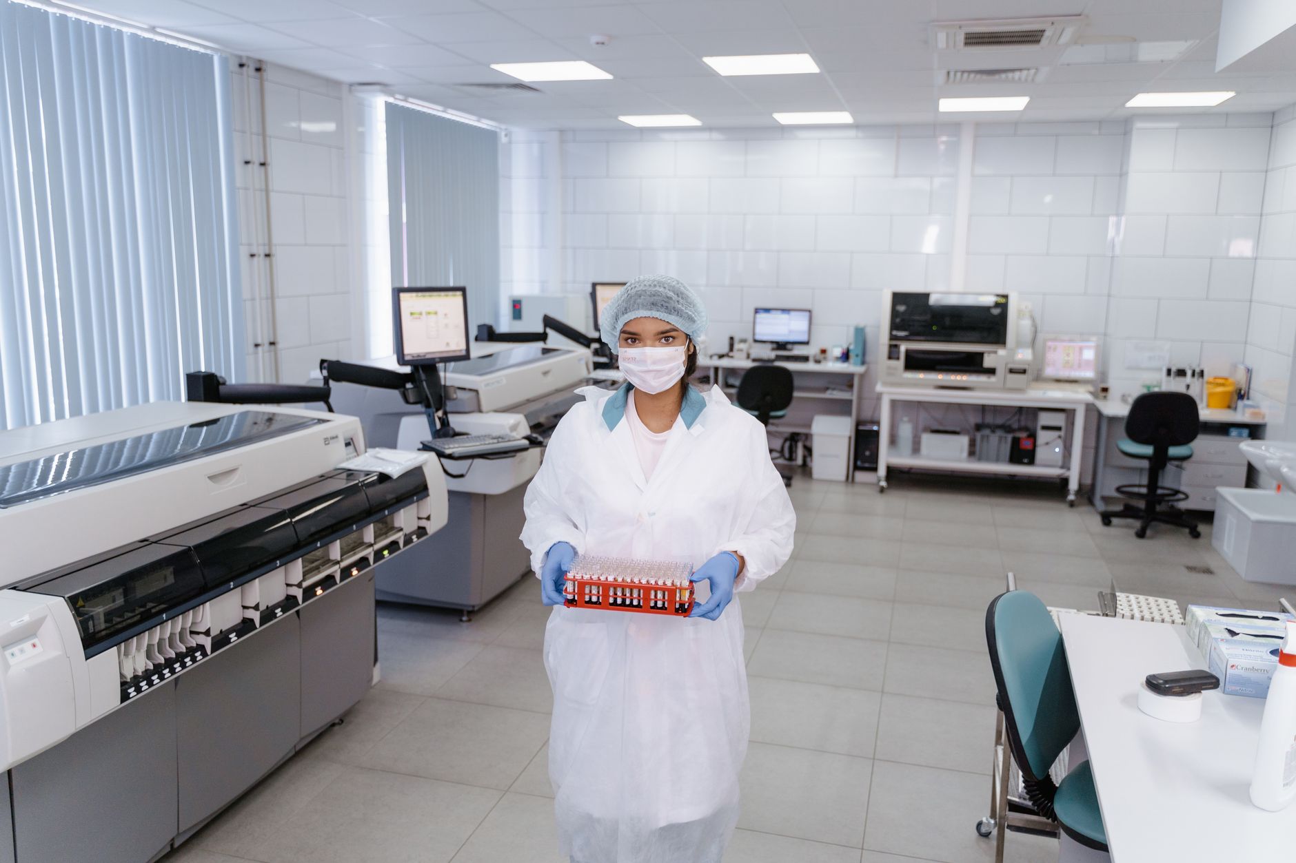 A laboratory technician in PPE holding a tray of samples in a modern sequencing lab.