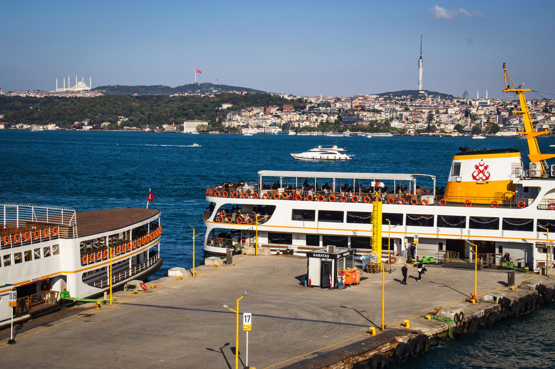 Boats docked at Kabataş Port in Istanbul, with passengers and distant city skyline.