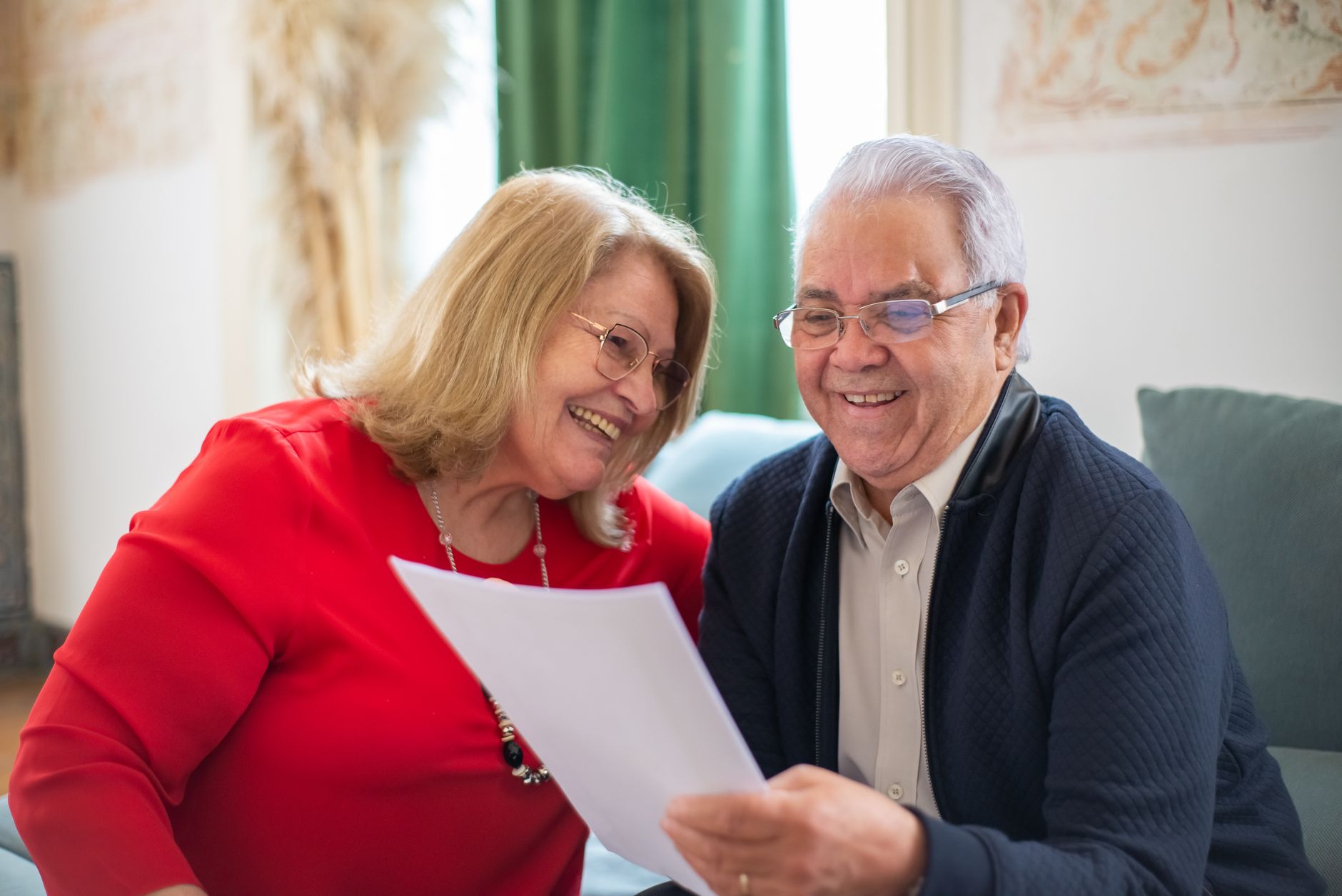 An elderly couple smiling while reviewing family history documents together at home.