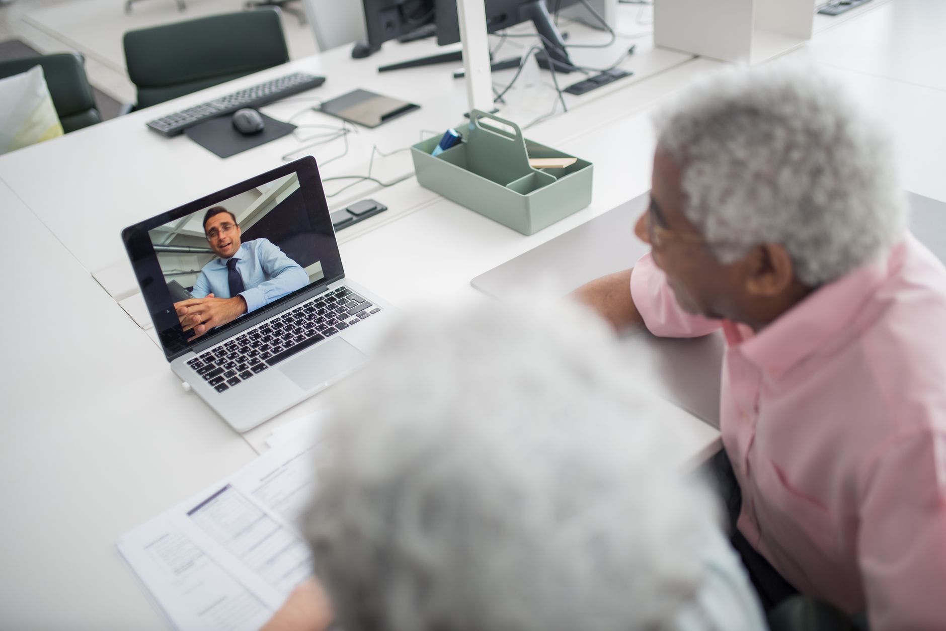 An elderly couple engages in a video consultation with a counselor on a laptop in a modern office.
