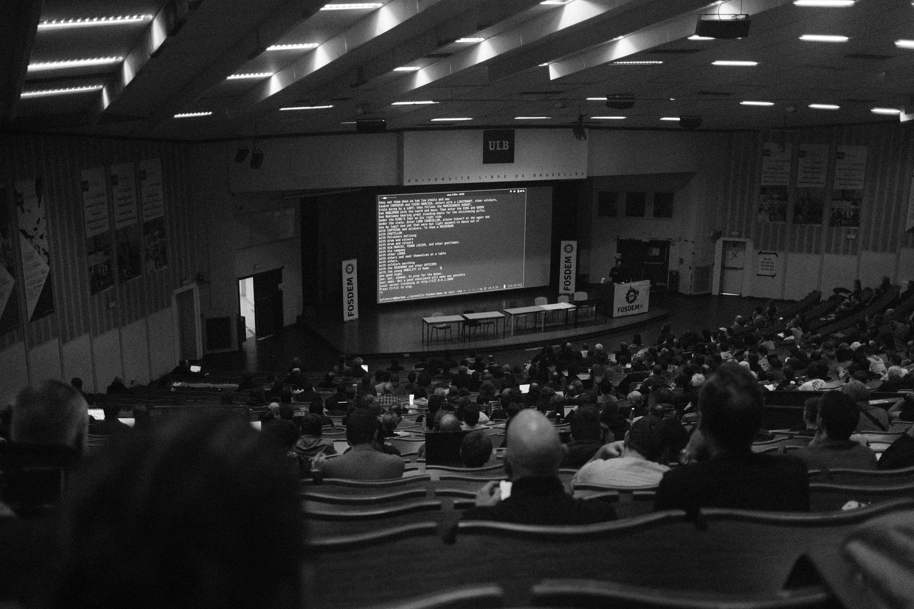 Attendees at FOSDEM 2023 in Brussels, focusing on a screen presentation.