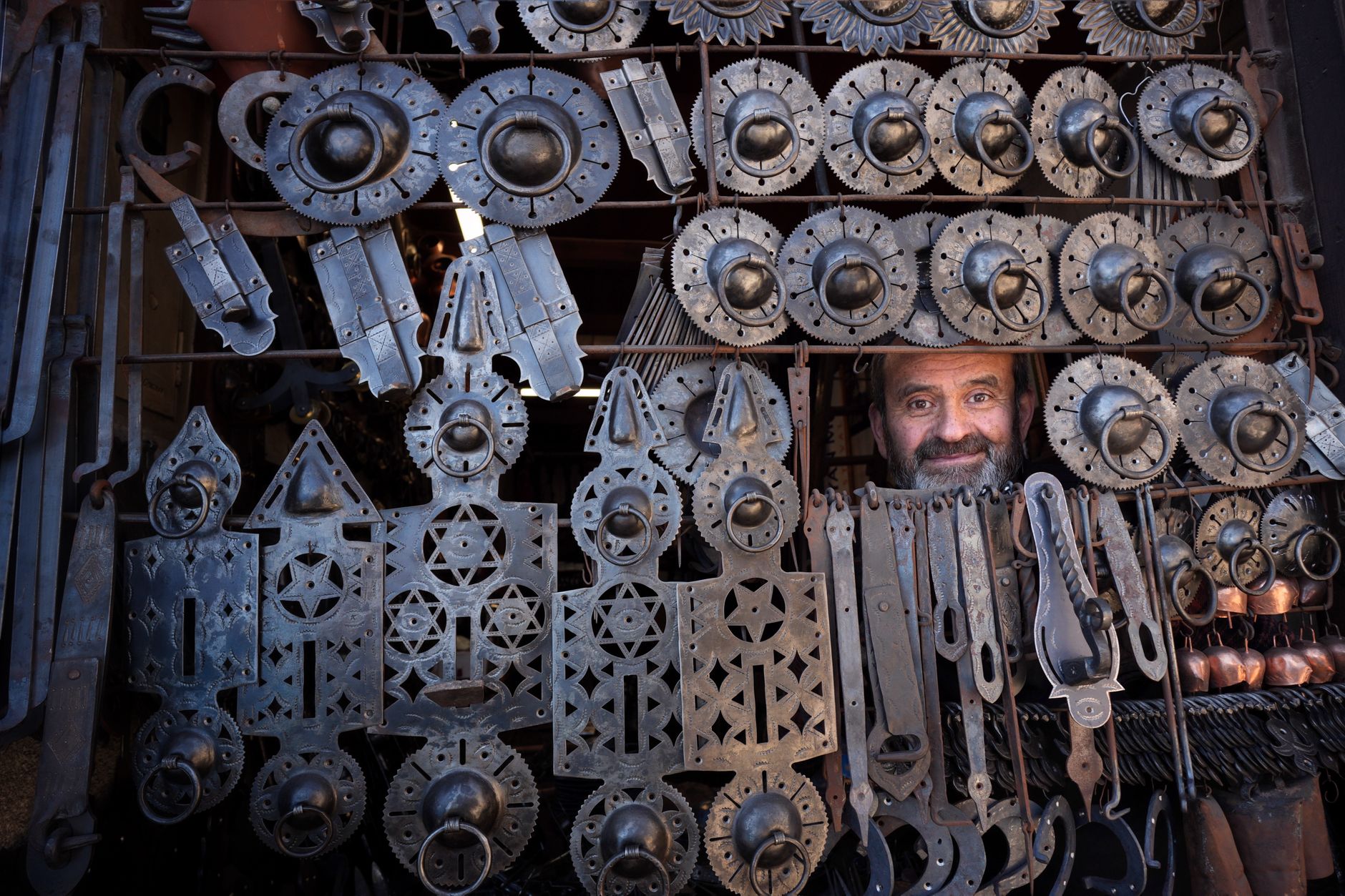 Bir çarşıda karmaşık metal işleriyle çevrili gülümseyen bir bakırcı.
