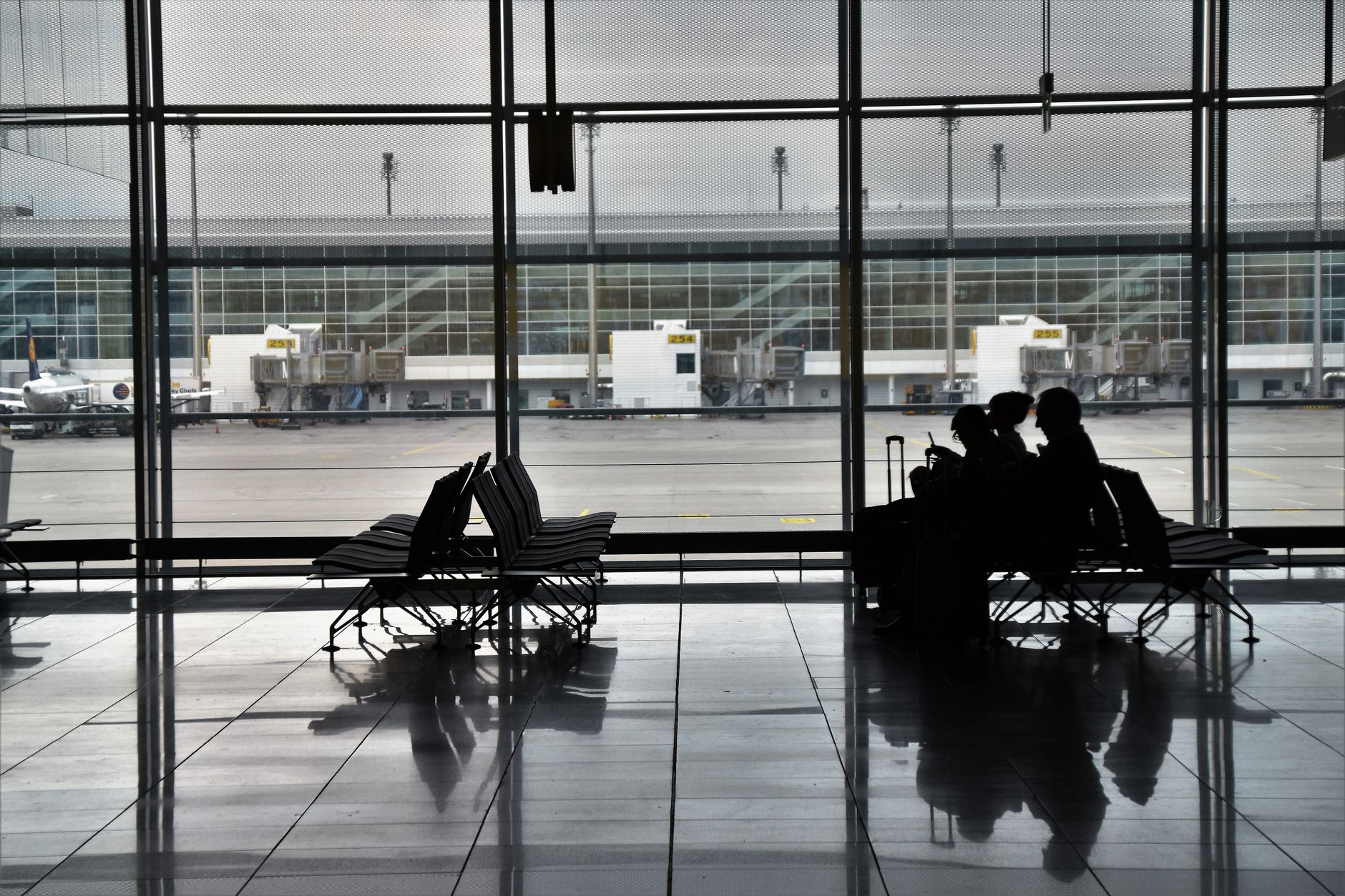 Silhouetted travelers sit in an airport waiting area with planes visible outside.