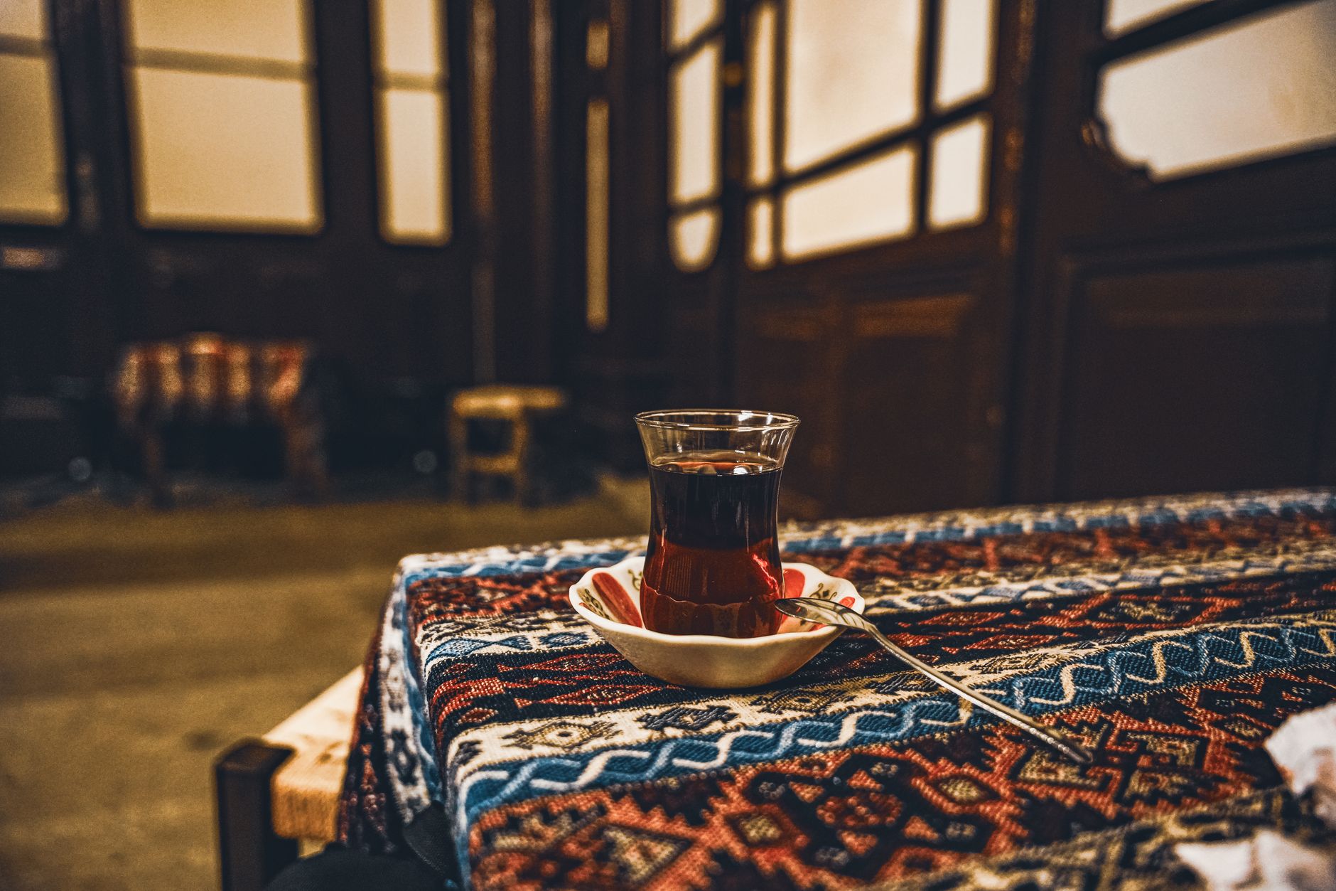 یک لیوان چای ترک روی رومیزی نقش‌دار در فضایی دنج و هنری.