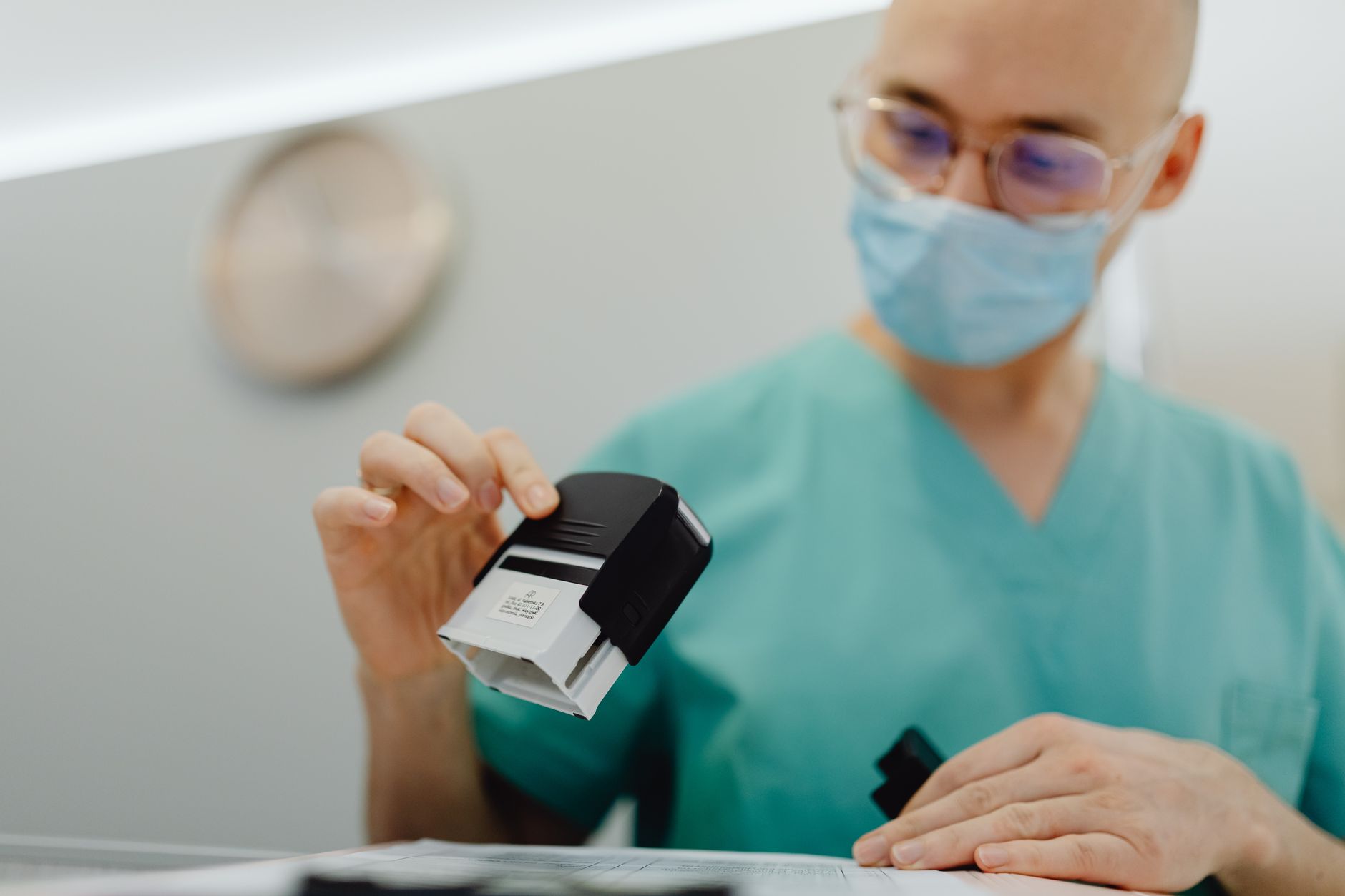 A healthcare professional in scrubs uses a stamp on a document, symbolizing certification.