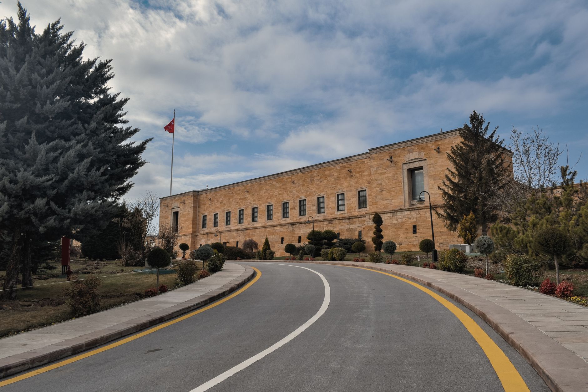 Exterior view of an official government building in Ankara, showcasing landscaped gardens and the Turkish flag.