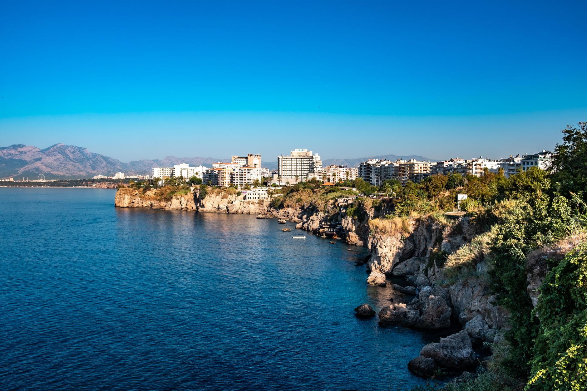 Panoramic view of Antalya's coastline featuring cliffs, cityscape, and clear blue waters.