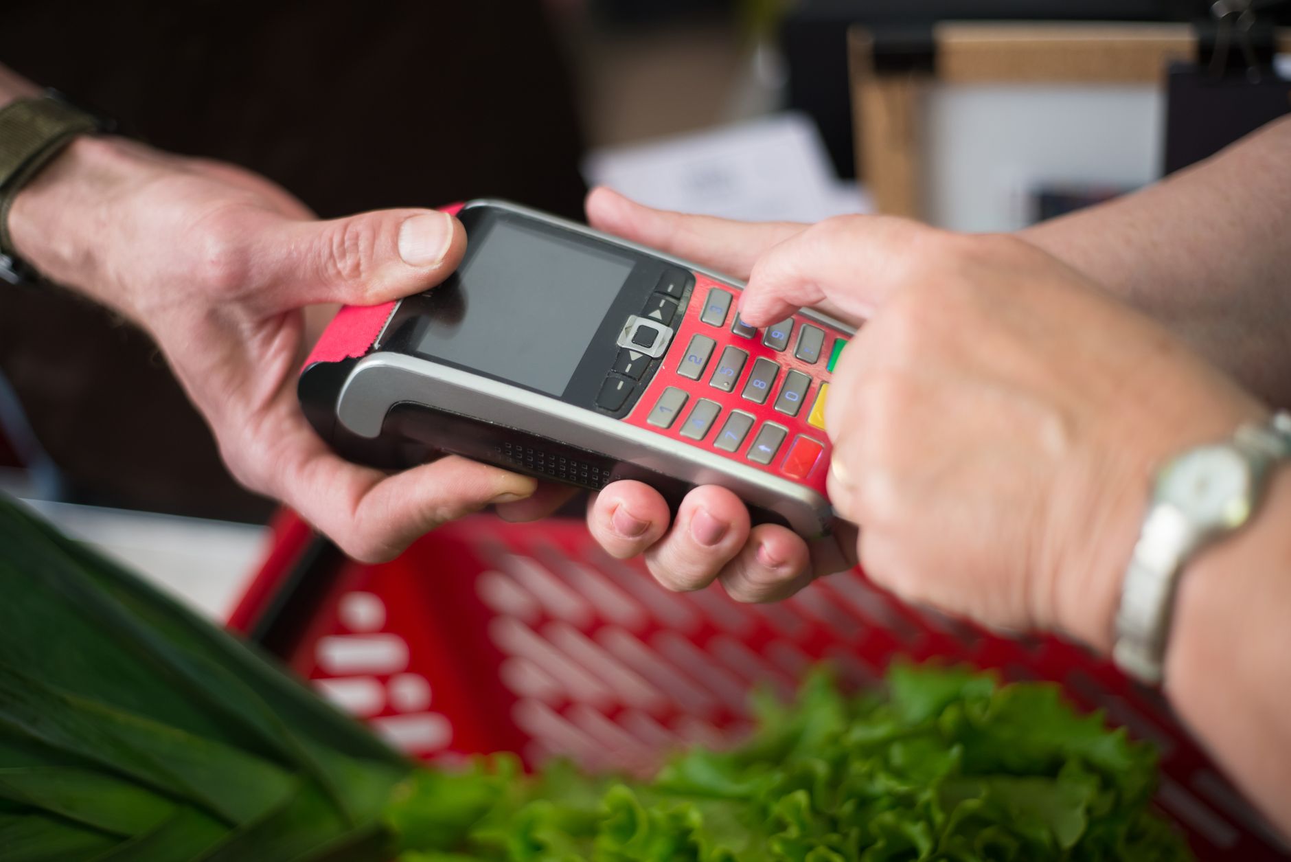 A person using a card payment terminal while checking out vegetables at a market.