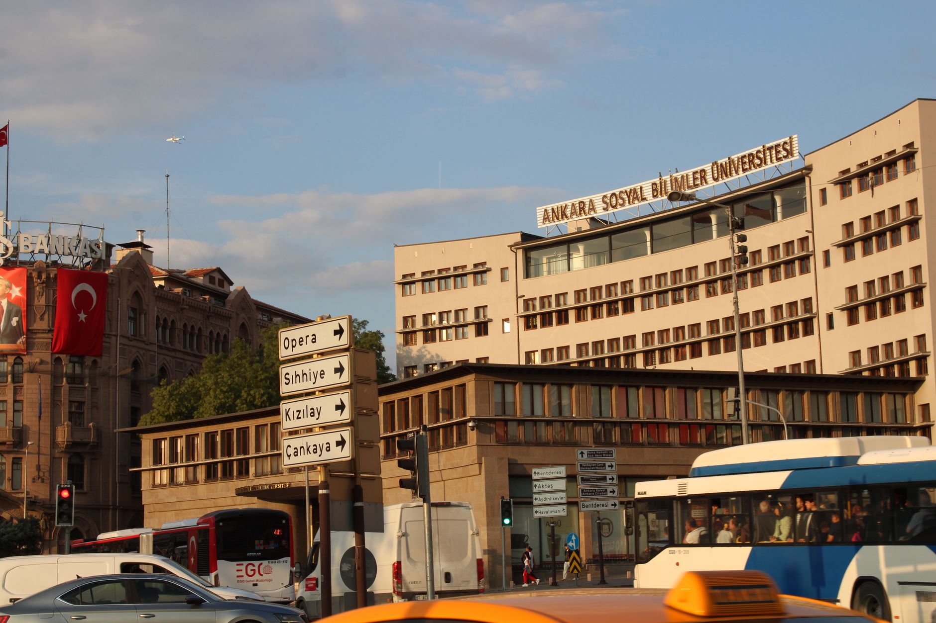 The facade of Ankara Social Sciences University with traffic signs directing to Opera, Kızılay, and other locations.