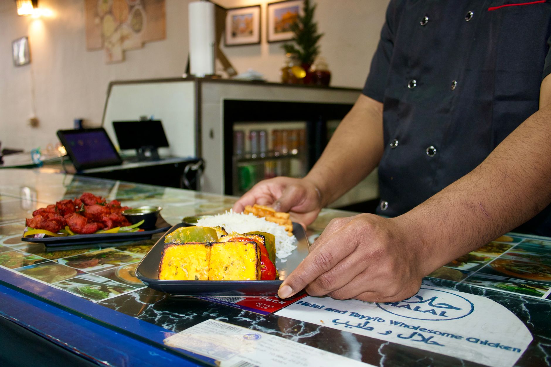 A chef serving colorful halal meal with rice and appetizers in a hospital setting.