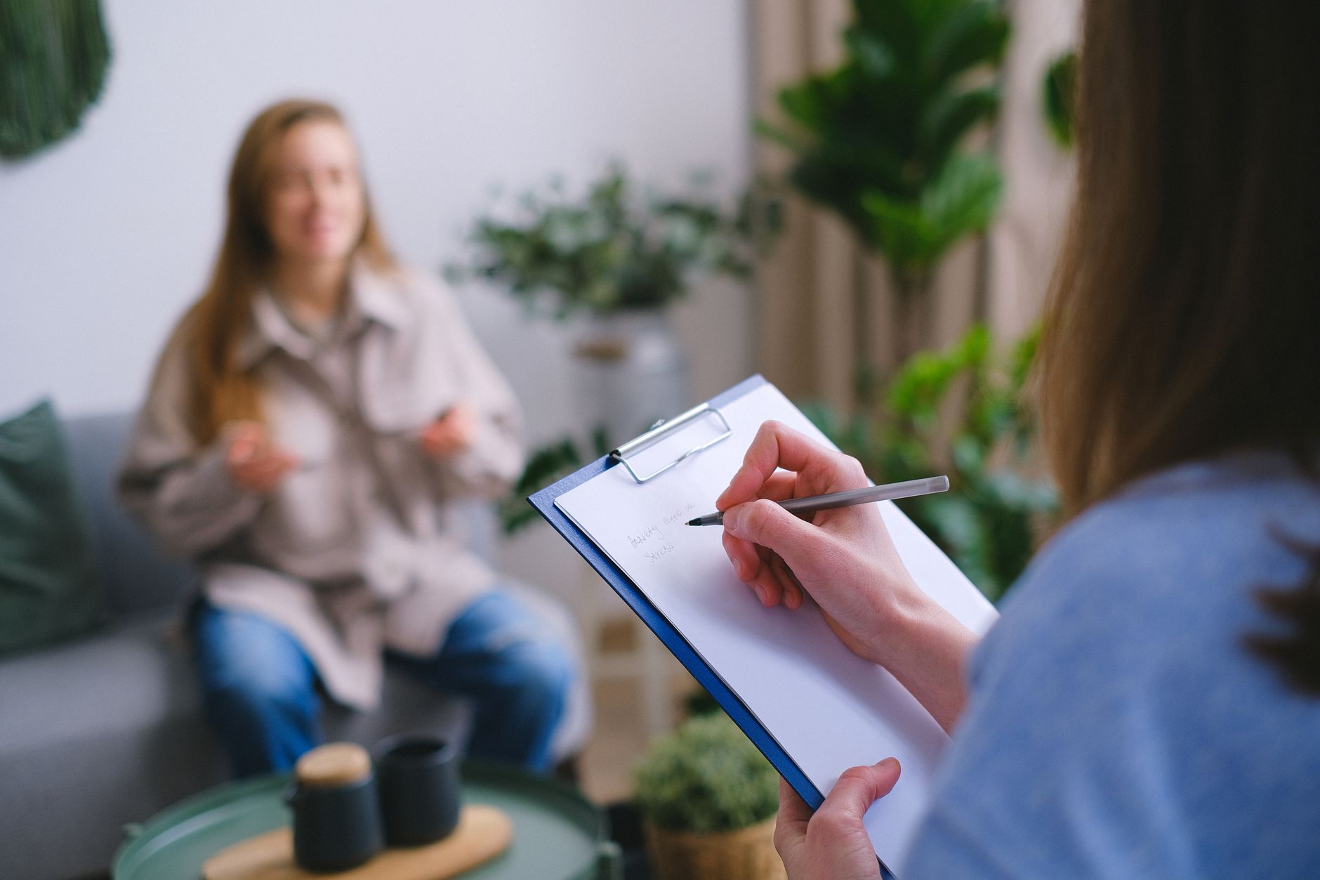 A person taking notes on a clipboard during an online medical consultation at home.