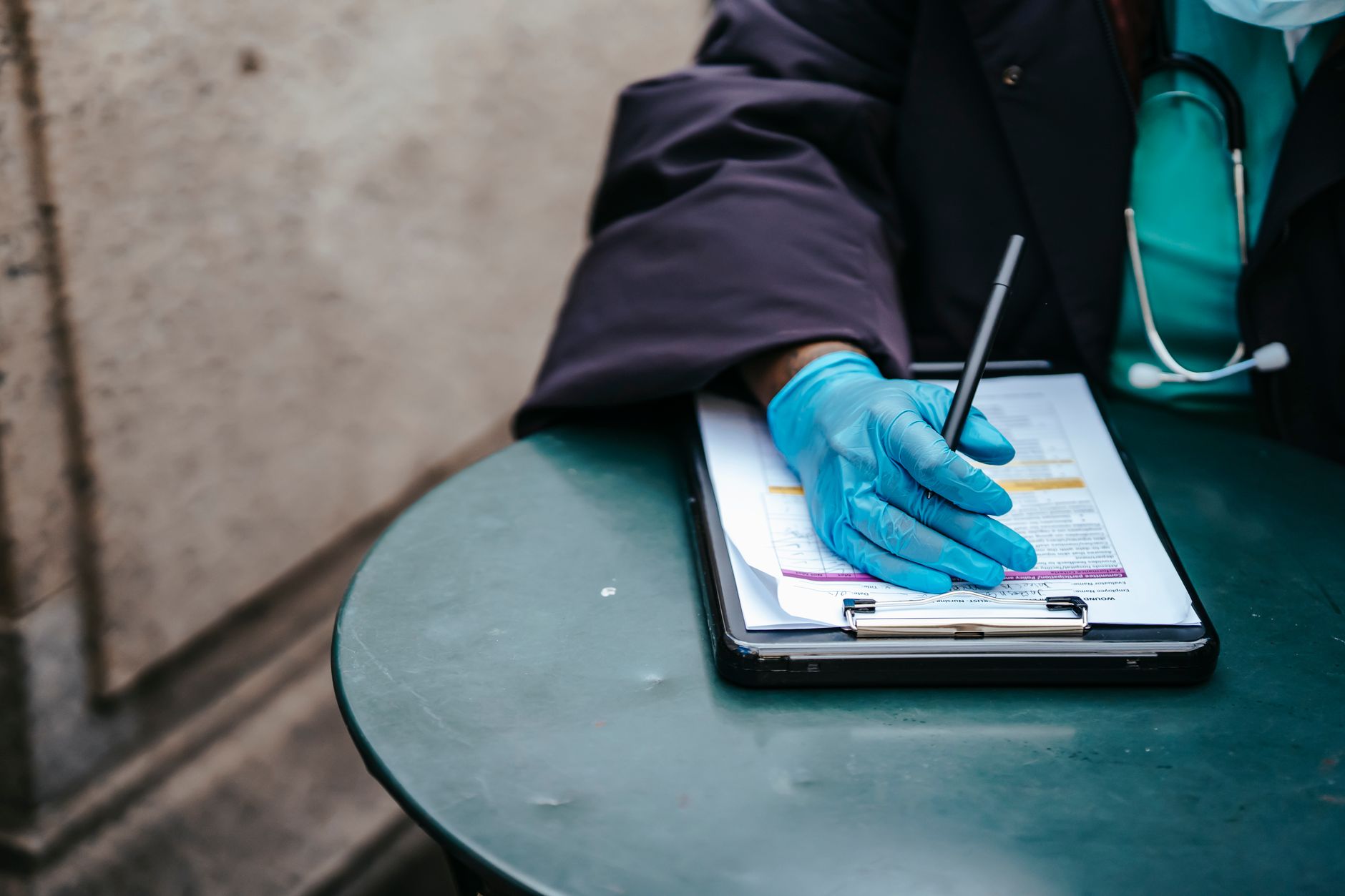 A close-up of a gloved hand writing on medical documents on a green table.