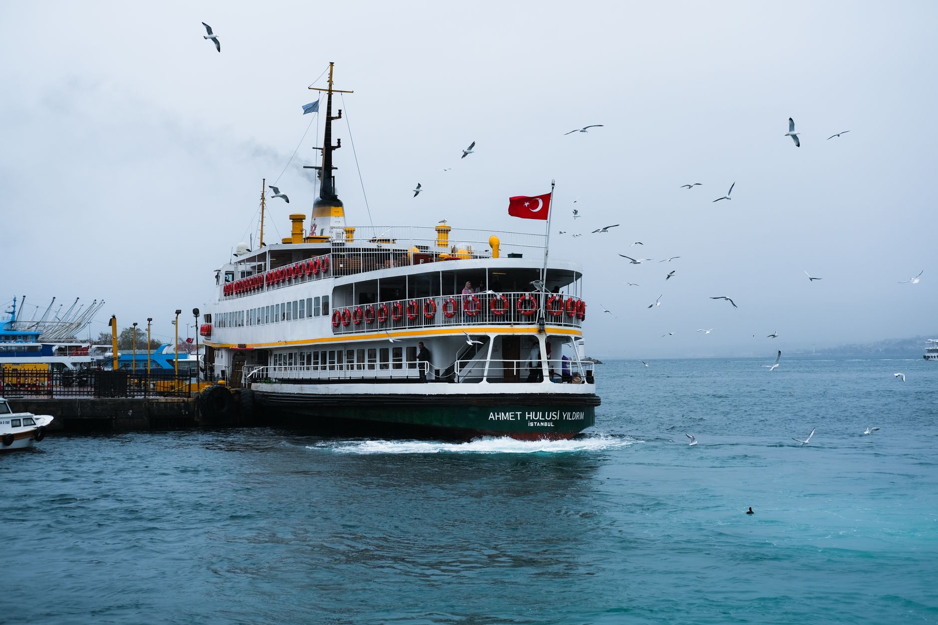A ferry named Ahmet Hulusi Yıldırım docked at Istanbul with seagulls flying around.