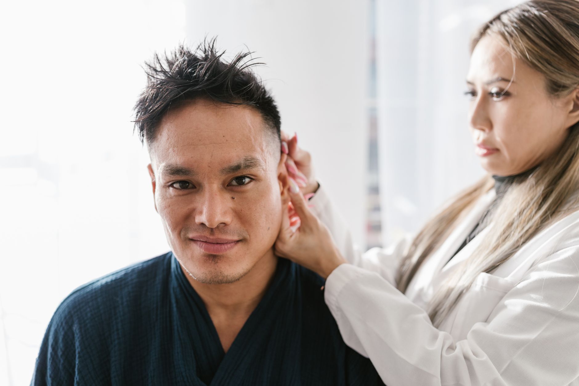 An audiologist adjusts a behind-the-ear hearing aid on a patient.