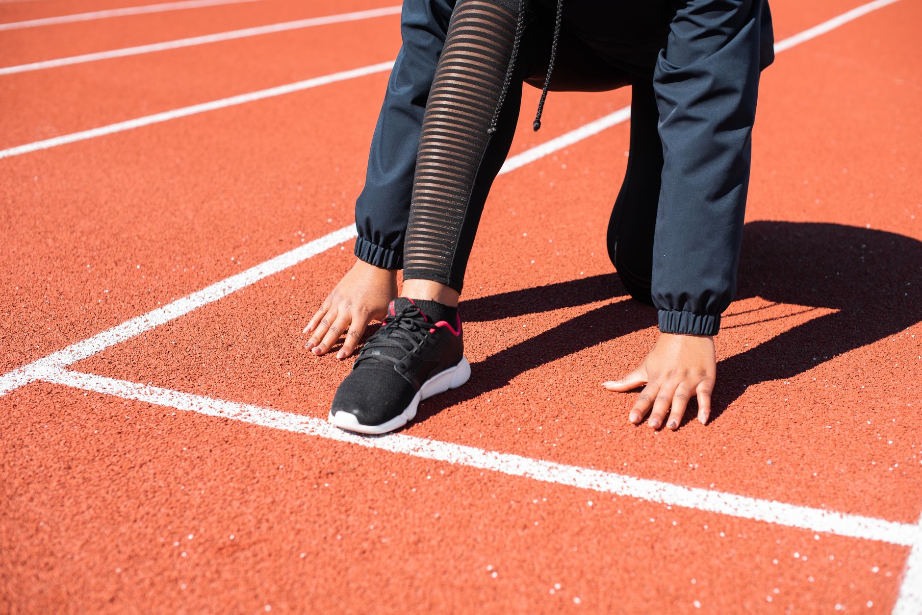 A runner is stretching on a red track, preparing for training after hip surgery.