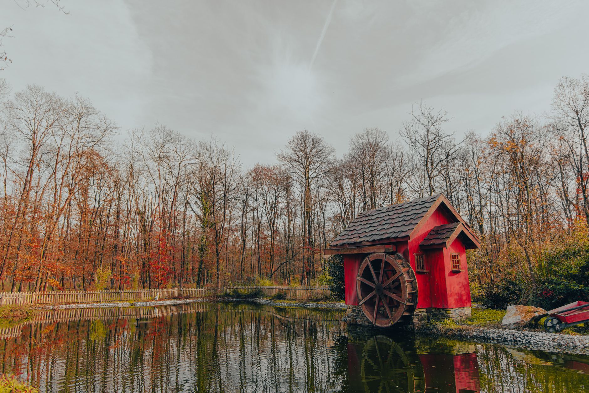 A picturesque old watermill with a wooden wheel beside a serene forest stream, surrounded by autumn foliage.
