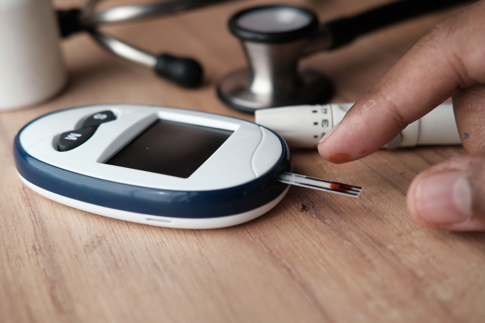 Close-up of a finger pricking a blood glucose meter on wooden surface.
