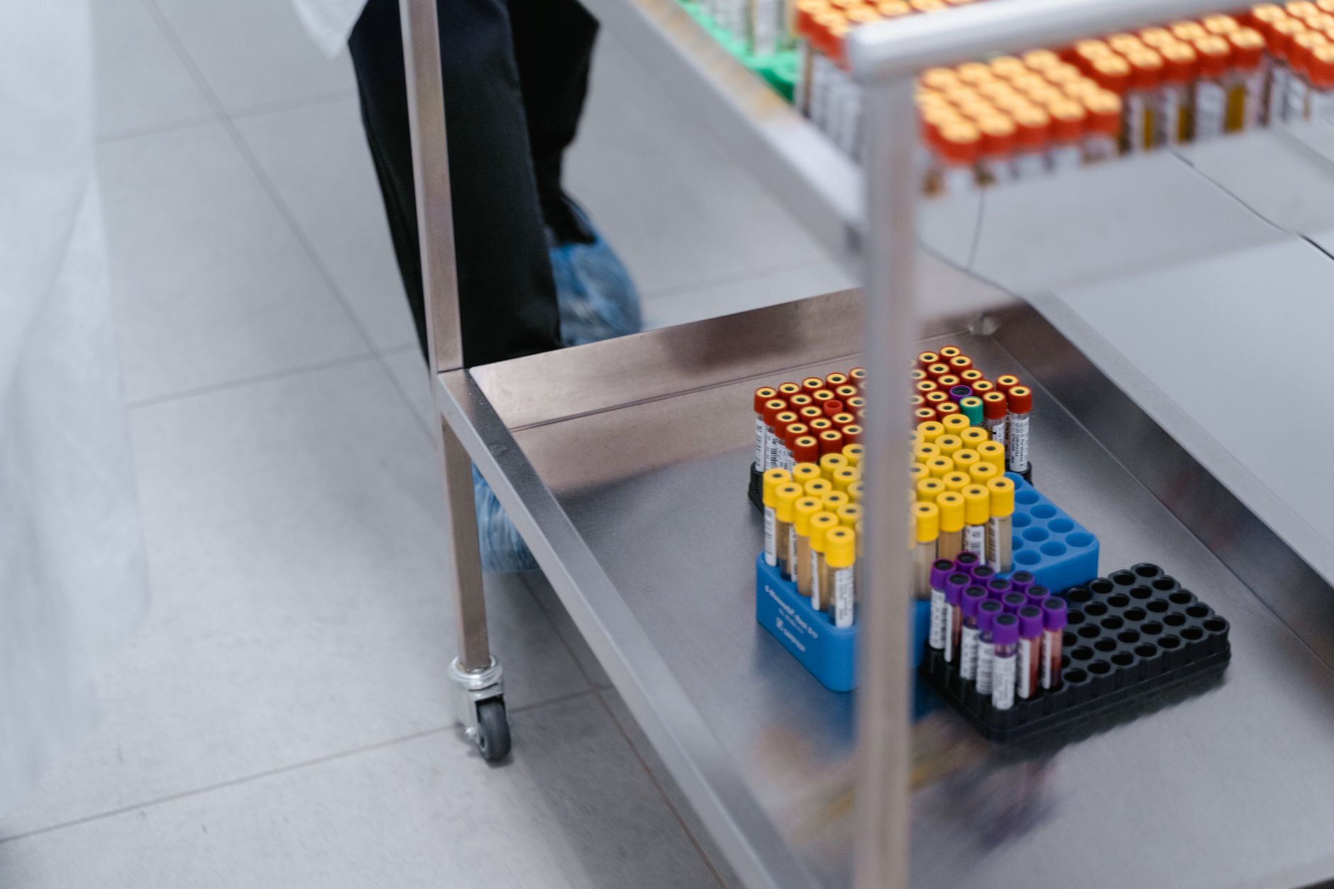 Various blood test tubes organized on a metal cart in a hospital lab.
