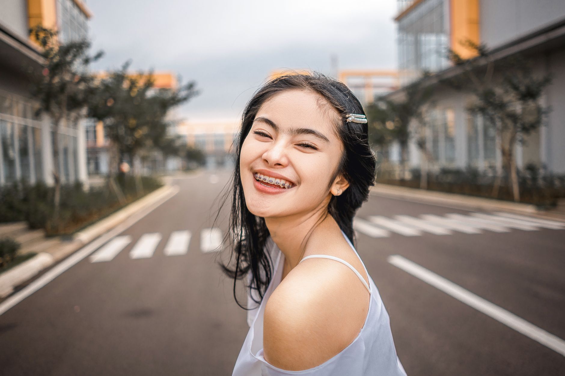 A smiling girl with braces stands in an urban setting, showcasing her orthodontic treatment.