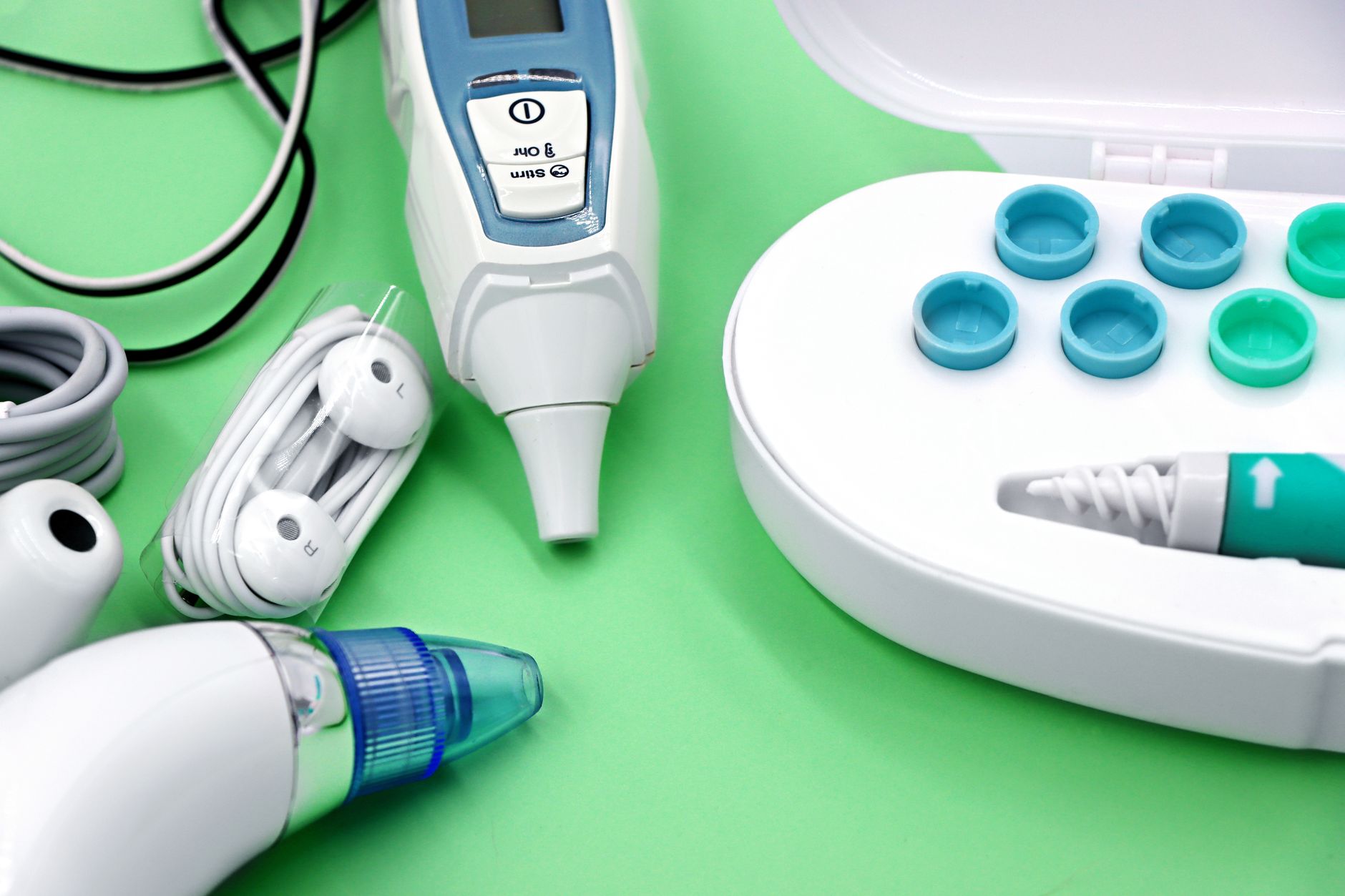 Close-up of various diagnostic devices including earphones and a thermometer, set on a green surface.