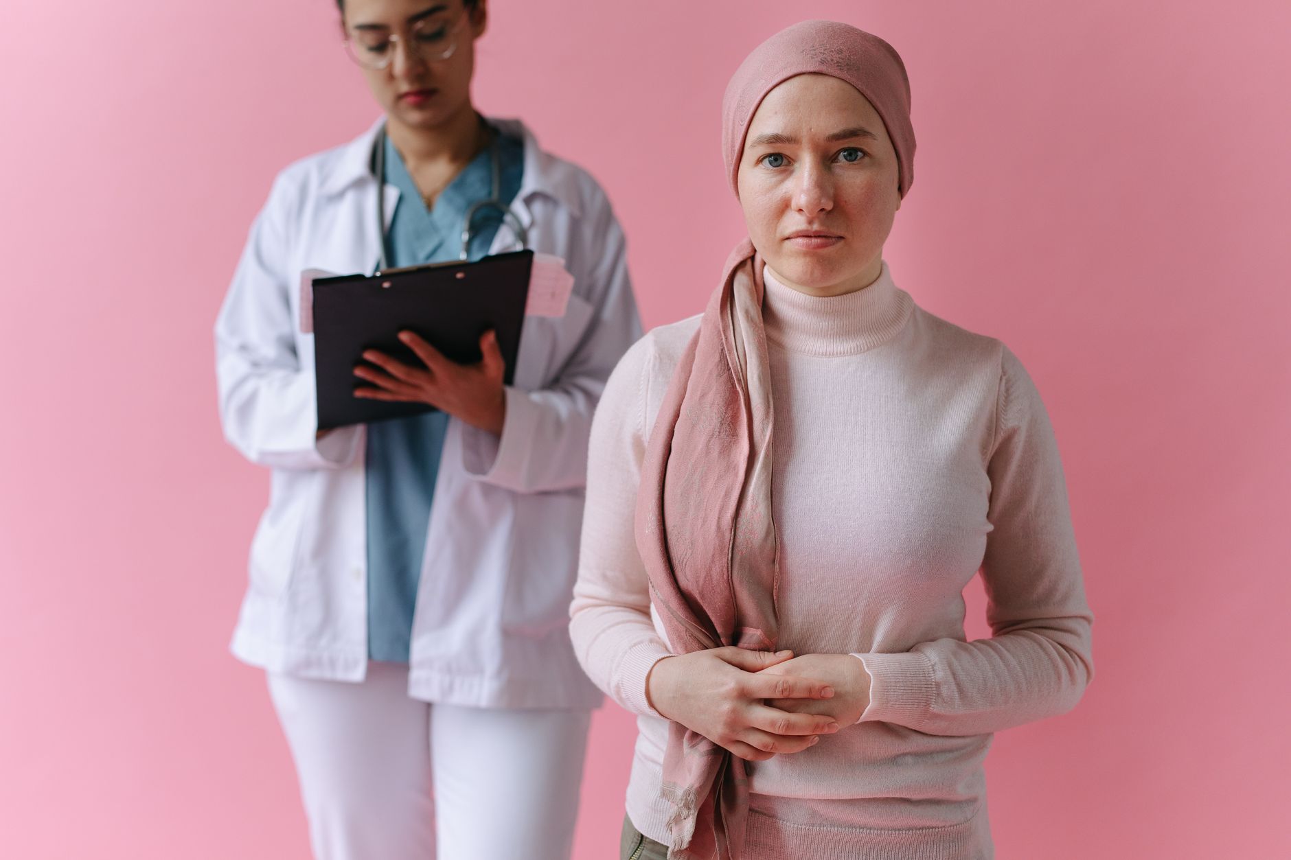 An oncology patient with a headscarf stands in front of a nurse in a day unit.