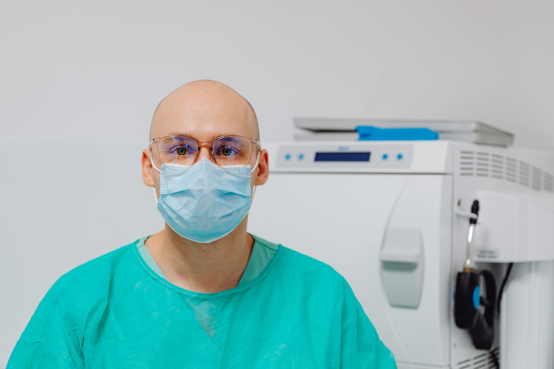 Close-up of a masked healthcare professional in scrubs beside HEPA filtration equipment.