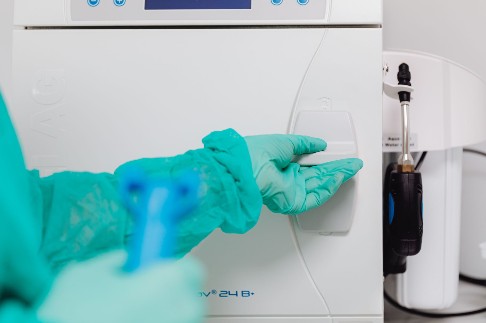 Close-up of a gloved hand operating a sterilization machine in a sterile processing department.