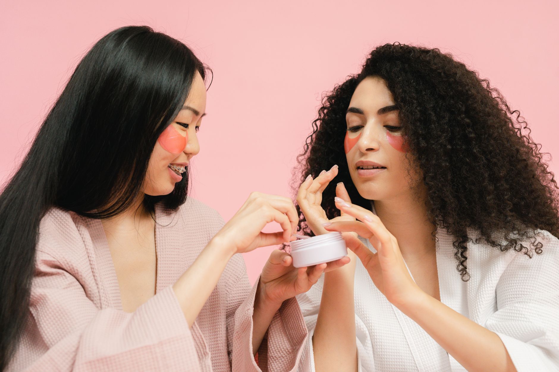 Two women enjoying a skincare session, applying products while smiling.
