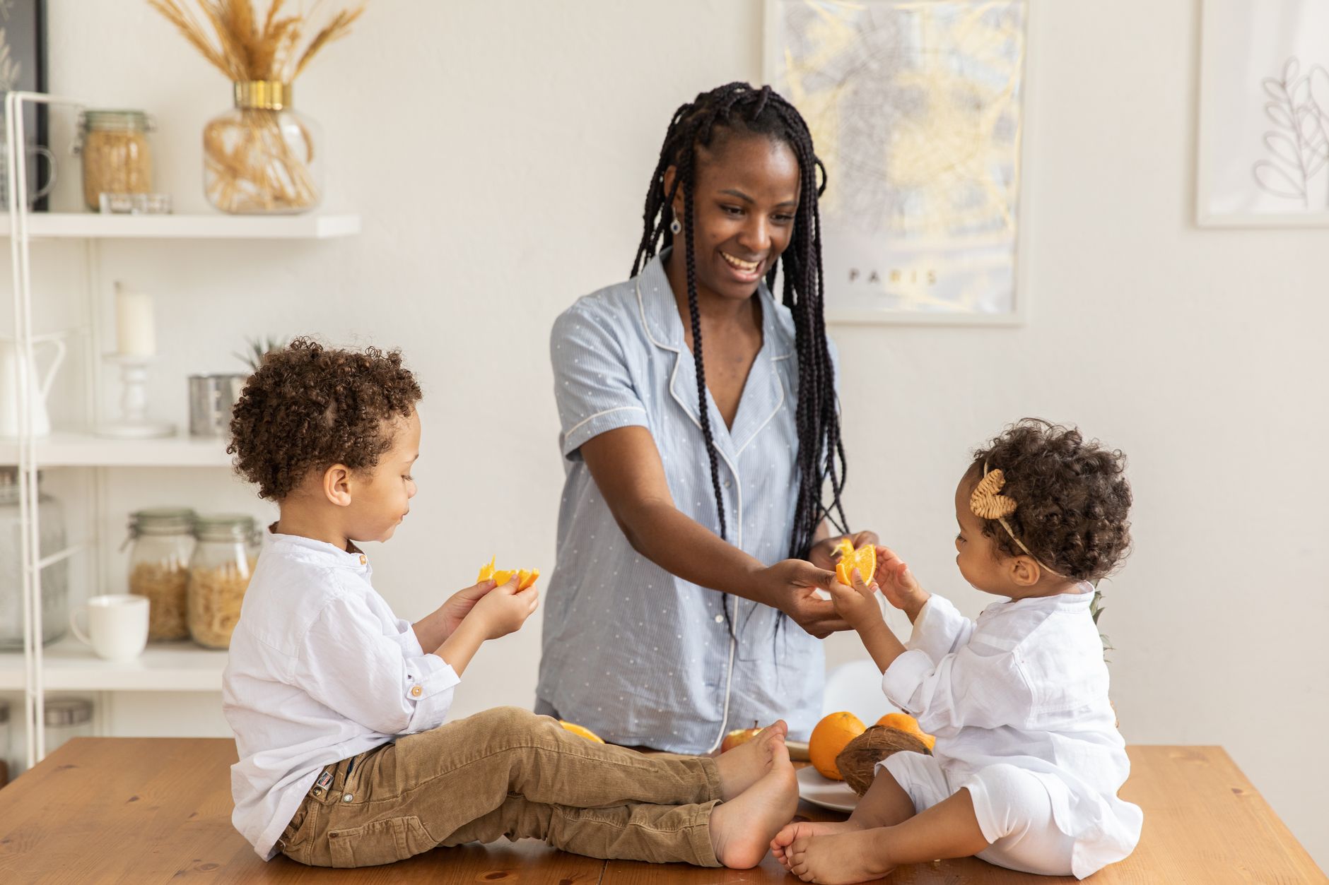 A mother engaging with her two children while preparing oranges in a cozy kitchen.