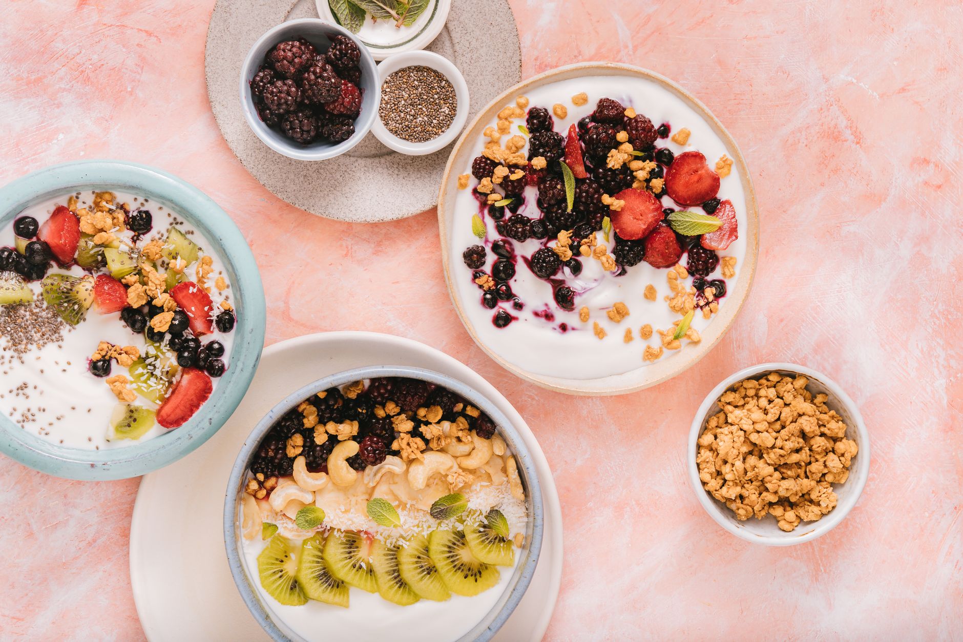 Three vibrant yogurt bowls topped with berries, kiwi, and granola.