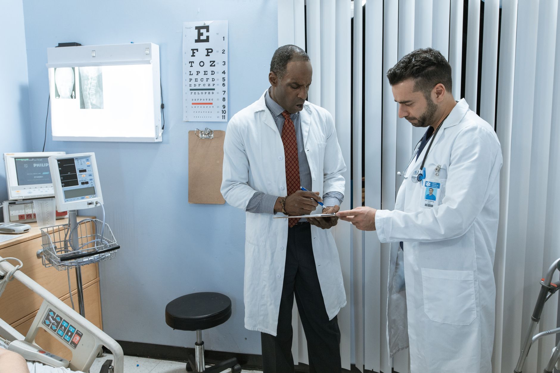 Two doctors reviewing pathology results in a hospital room, with medical equipment and an X-ray on the wall.