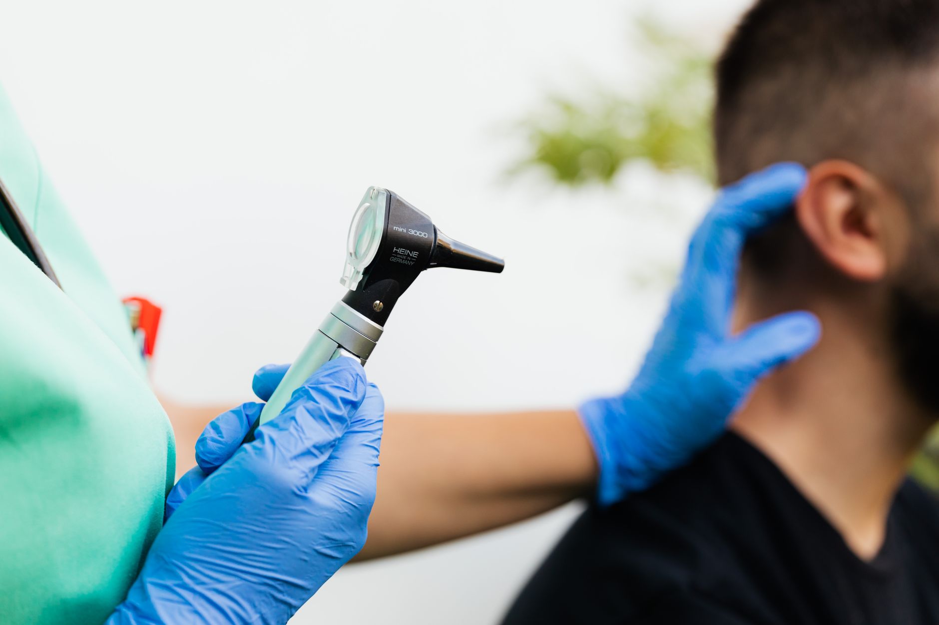 An audiologist with blue gloves using an otoscope on a patient's ear.