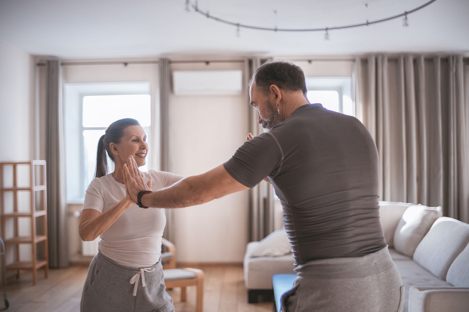A smiling couple engaged in balance exercises indoors, demonstrating focus and connection.