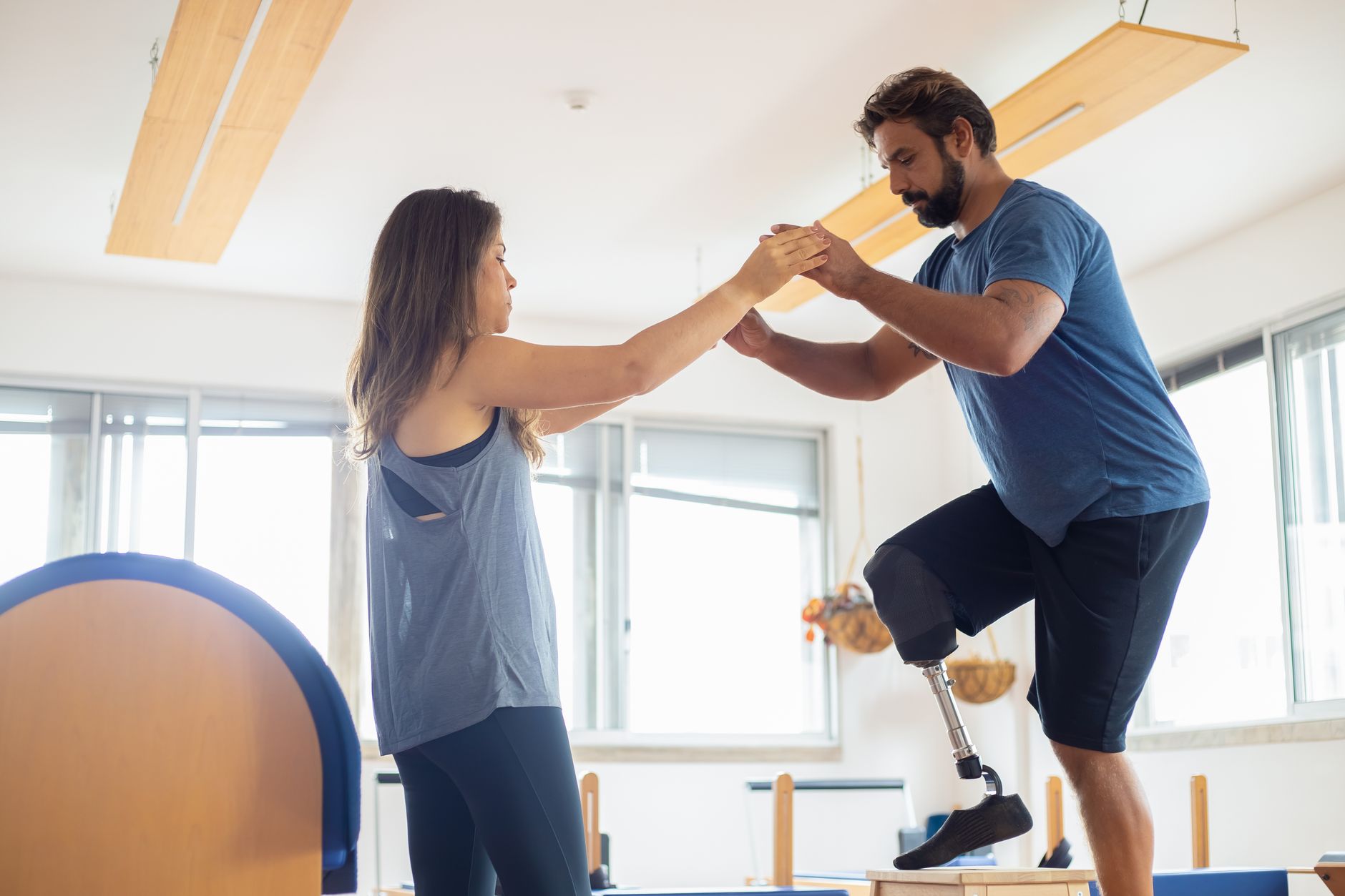 A therapist helps a patient with a prosthetic leg during balance exercises in a rehabilitation gym.