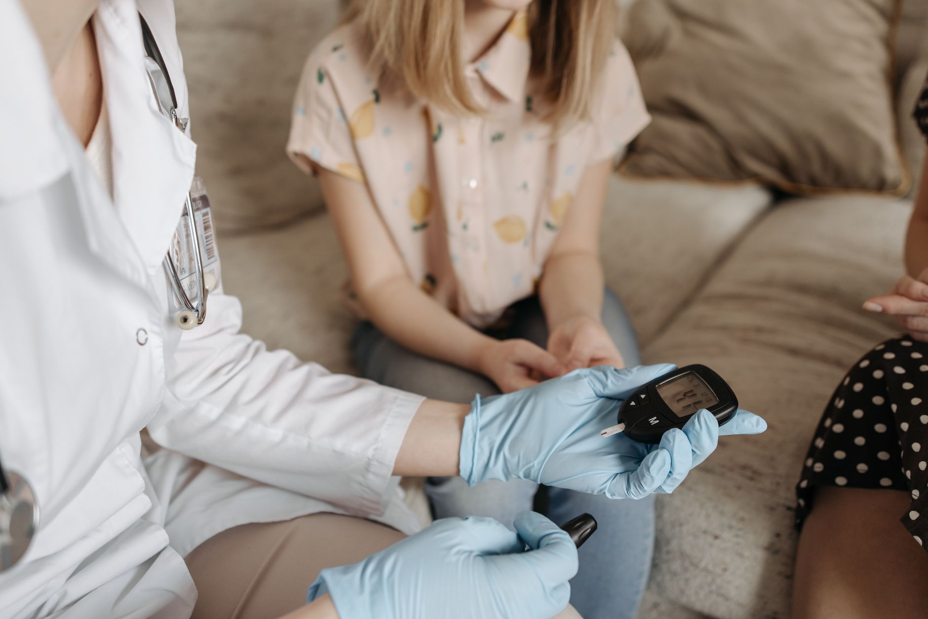 A nurse in gloves using a glucose meter on a patient's finger for blood sugar monitoring.