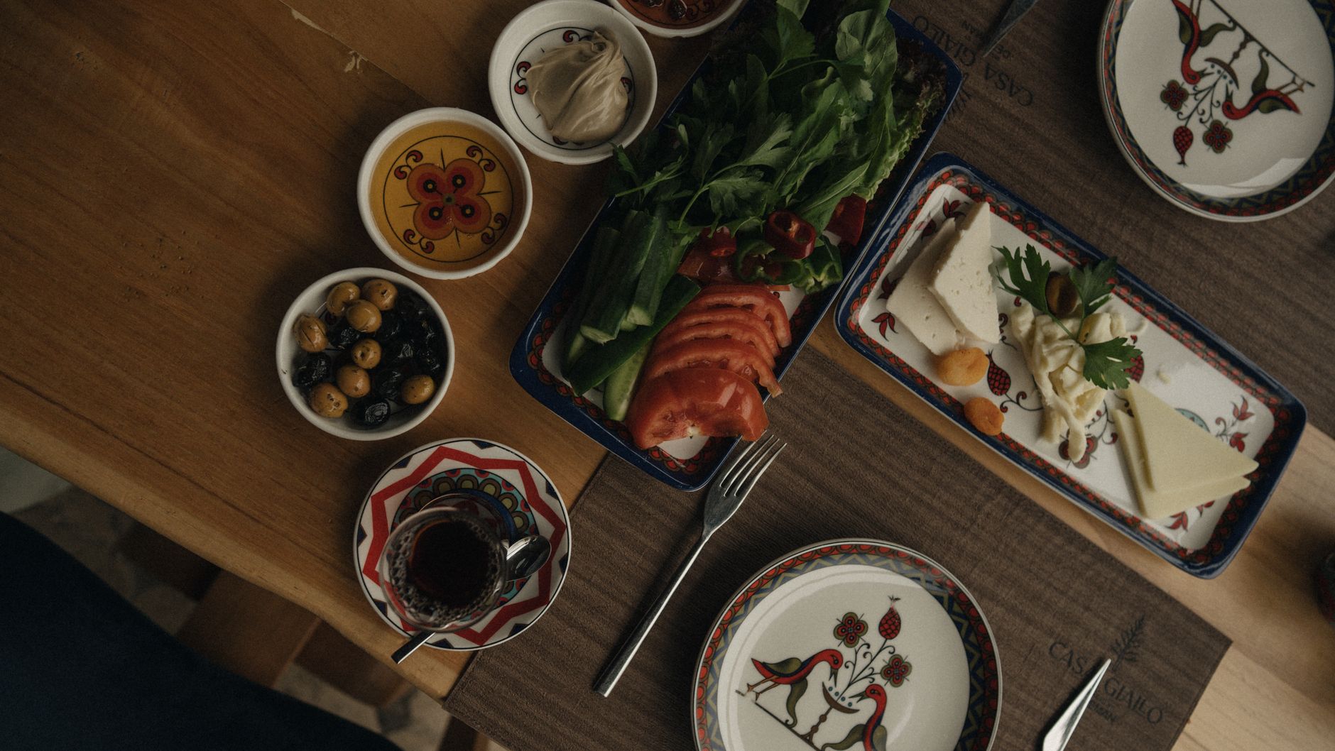 A vibrant Turkish meal with fresh vegetables, olives, cheese, and tea on a wooden table.