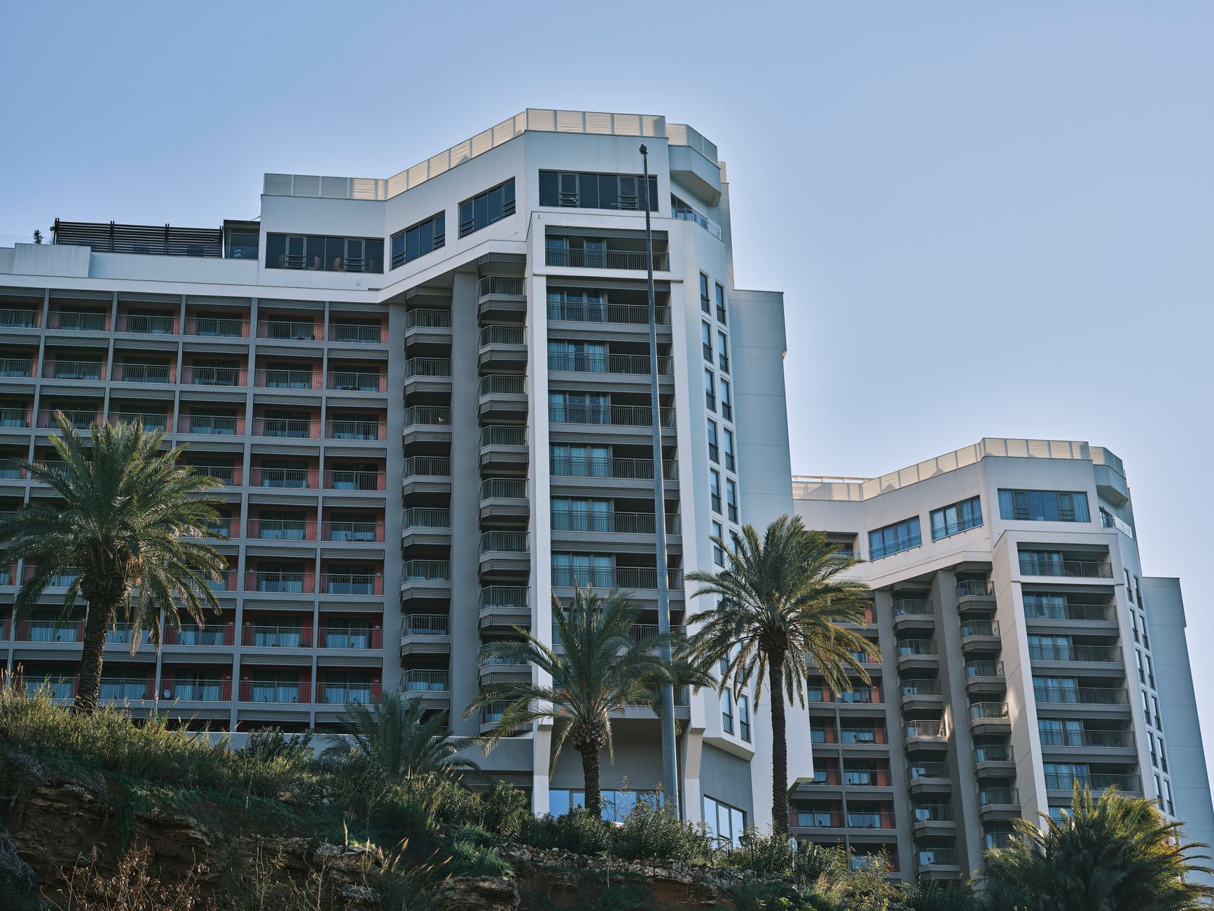 Exterior view of a modern hospital building in Antalya, surrounded by palm trees.