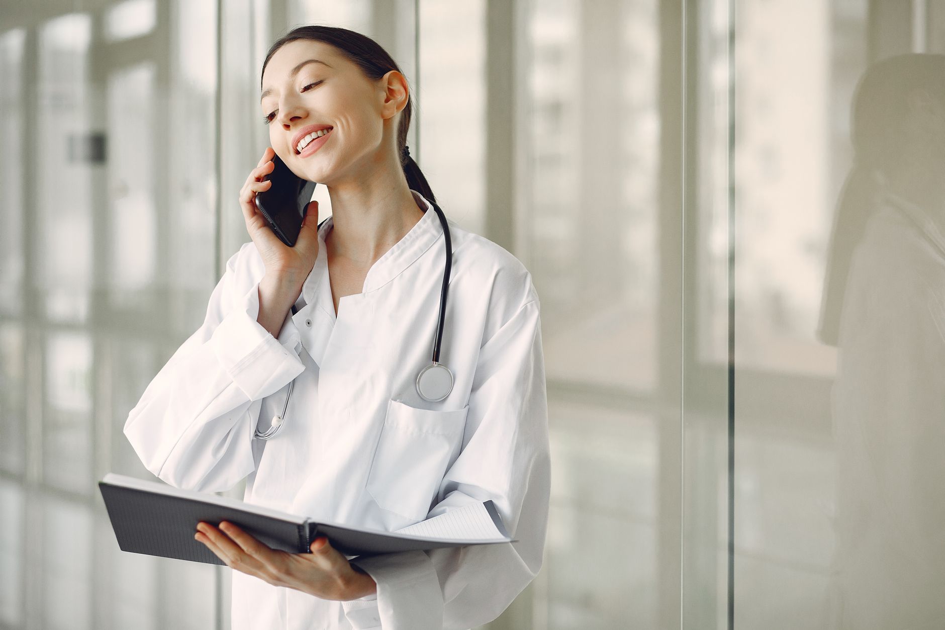 A medical interpreter in a white coat communicates on the phone while holding a notebook.