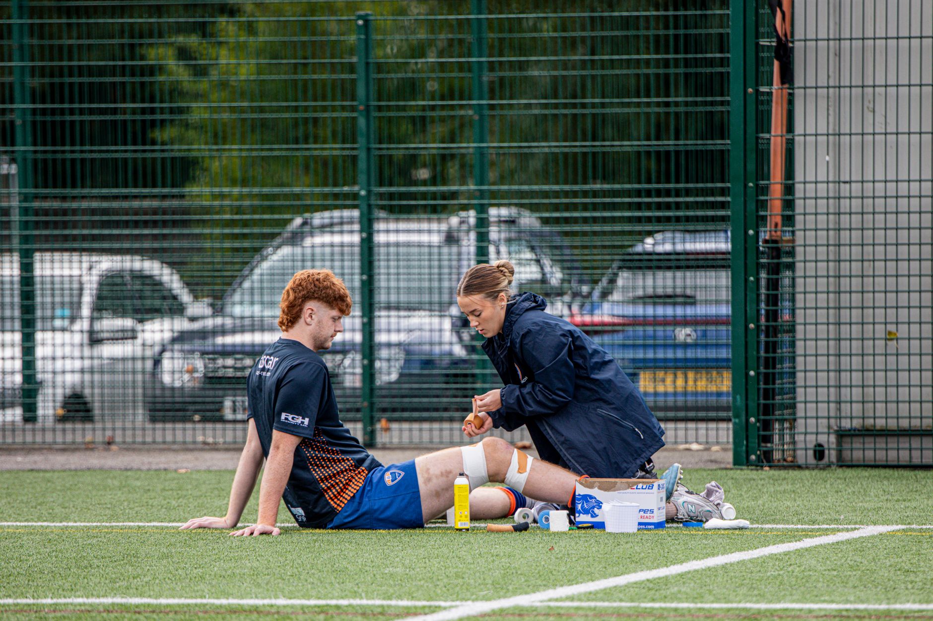 A female sports therapist treating an athlete's knee injury on a field.