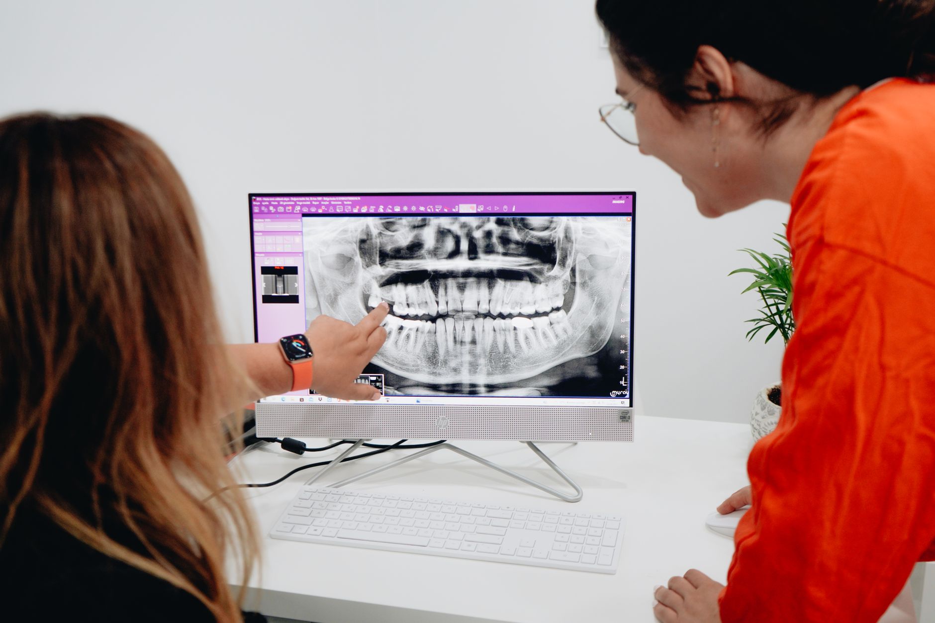 A dentist points at a dental X-ray on a computer screen while discussing with a patient.