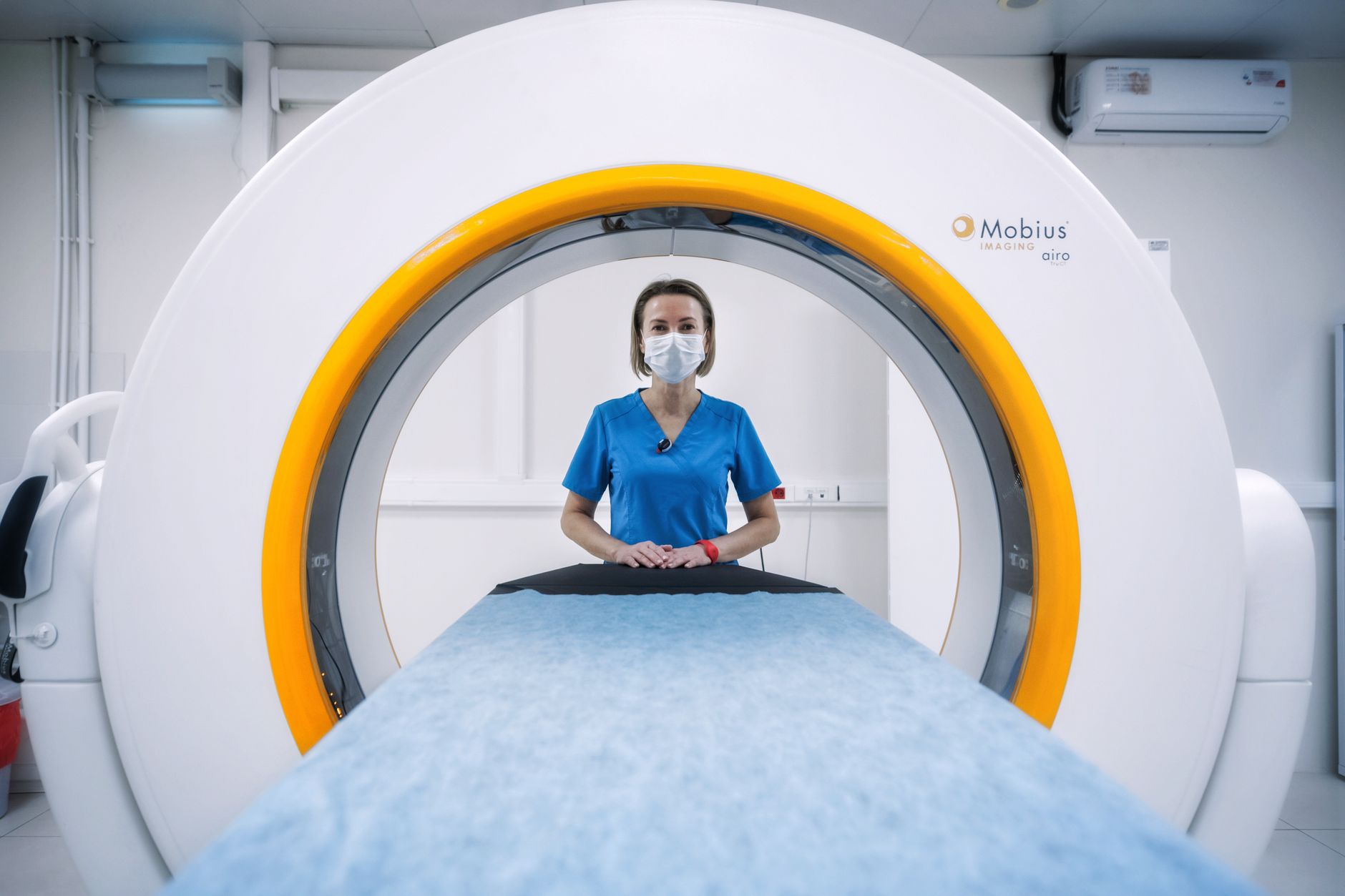 Medical professional in blue scrubs near a CT scanner, ready for imaging procedure.