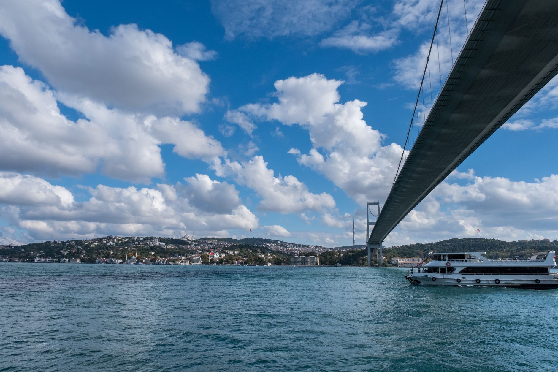 A panoramic view of Istanbul's waterfront featuring a bridge, clouds, and a boat, highlighting the city's beauty.